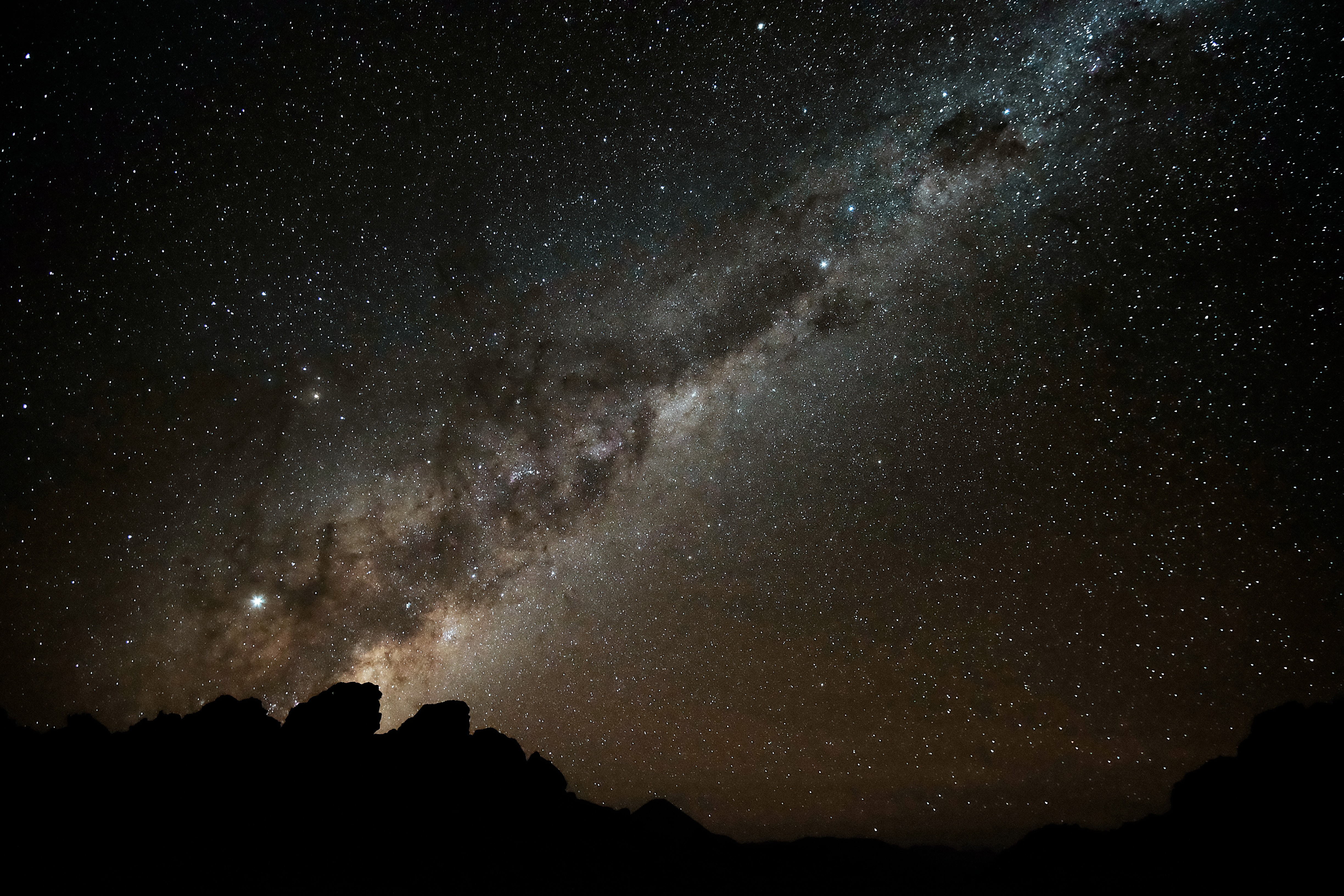 Milky Way stretches across a dark night sky above rocky silhouettes, with countless stars scattered over the horizon at night.
