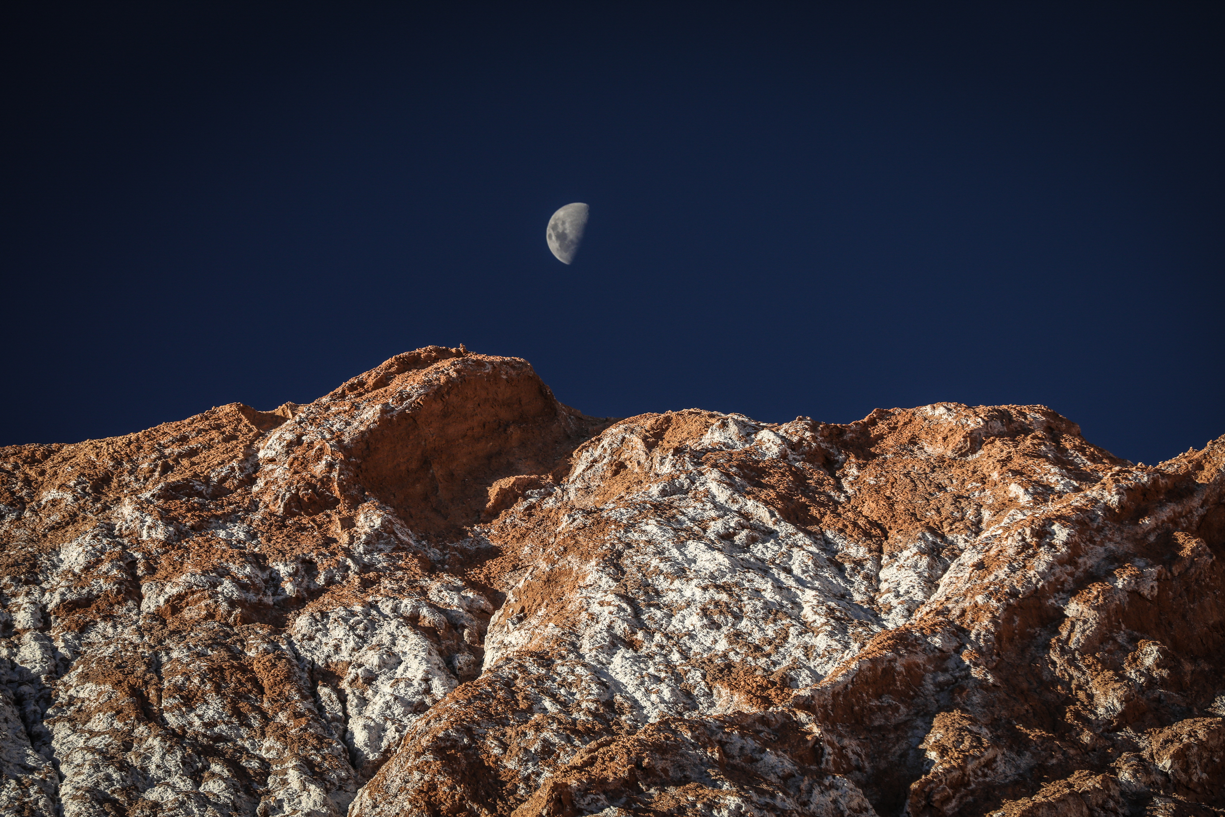Night scene shows a bright moon above rugged rocks, with deep blue sky and faint stars over desert terrain below.