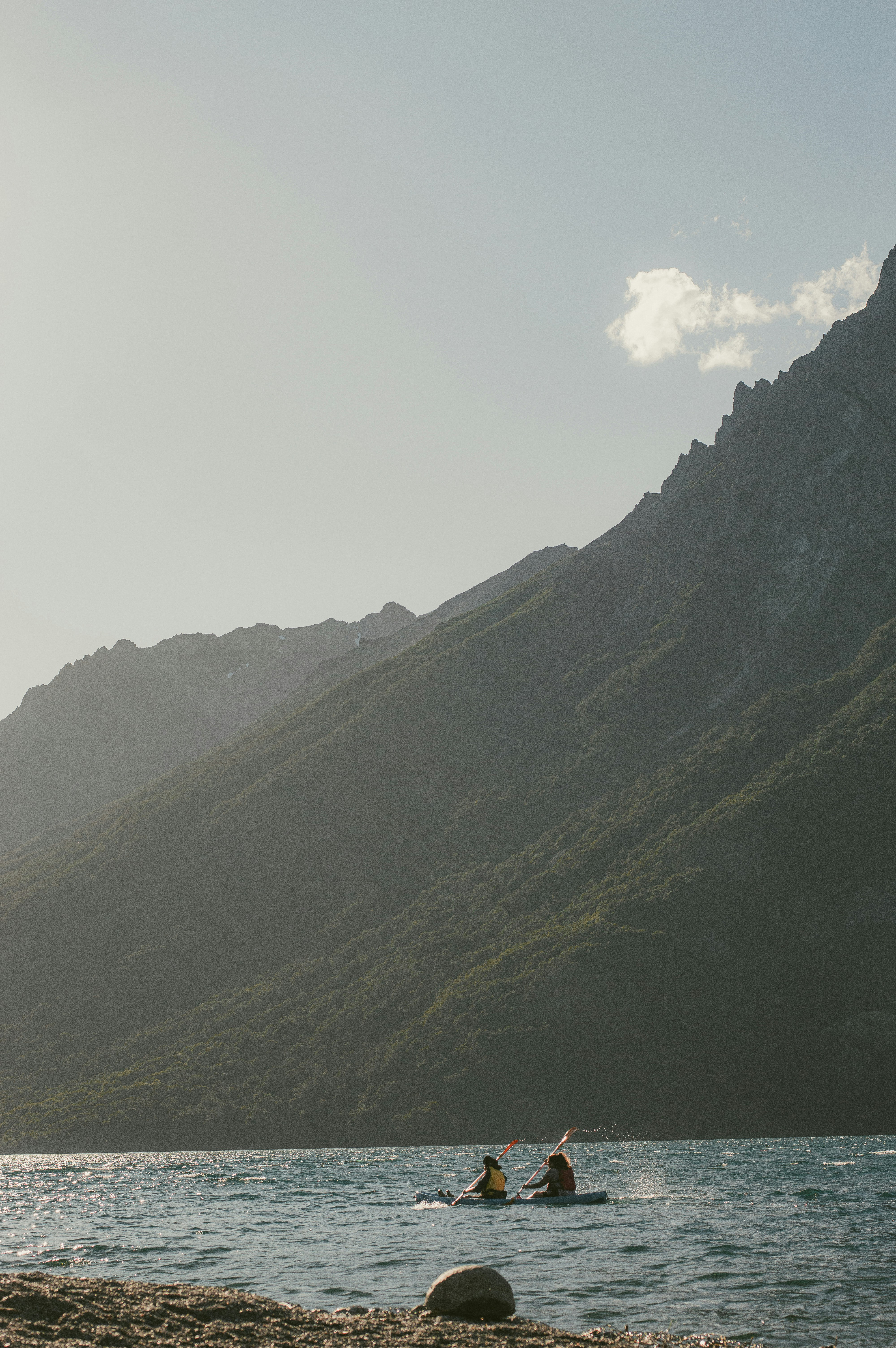 Small boat floats on a calm mountain lake between steep dark slopes, with misty light filtering through clouds above it.