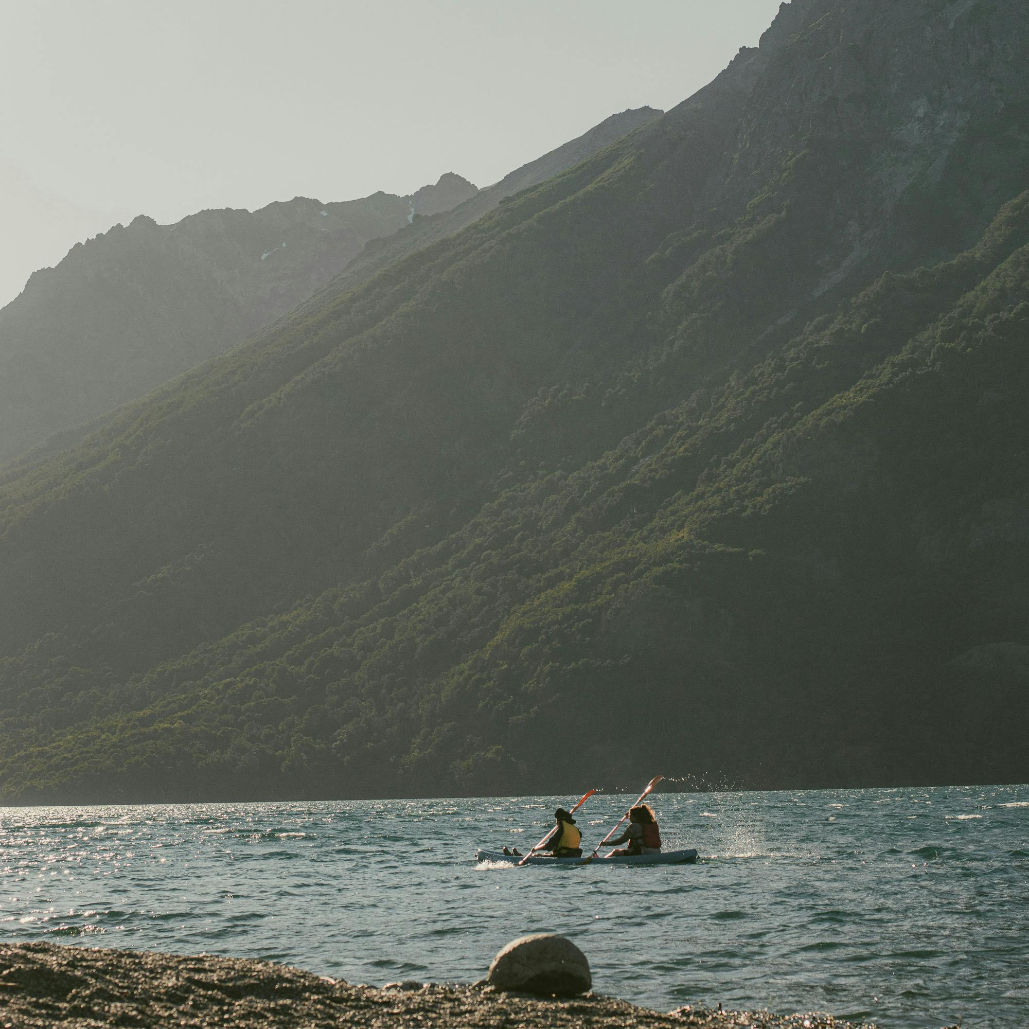 Small boat floats on a calm mountain lake between steep dark slopes, with misty light filtering through clouds above it.