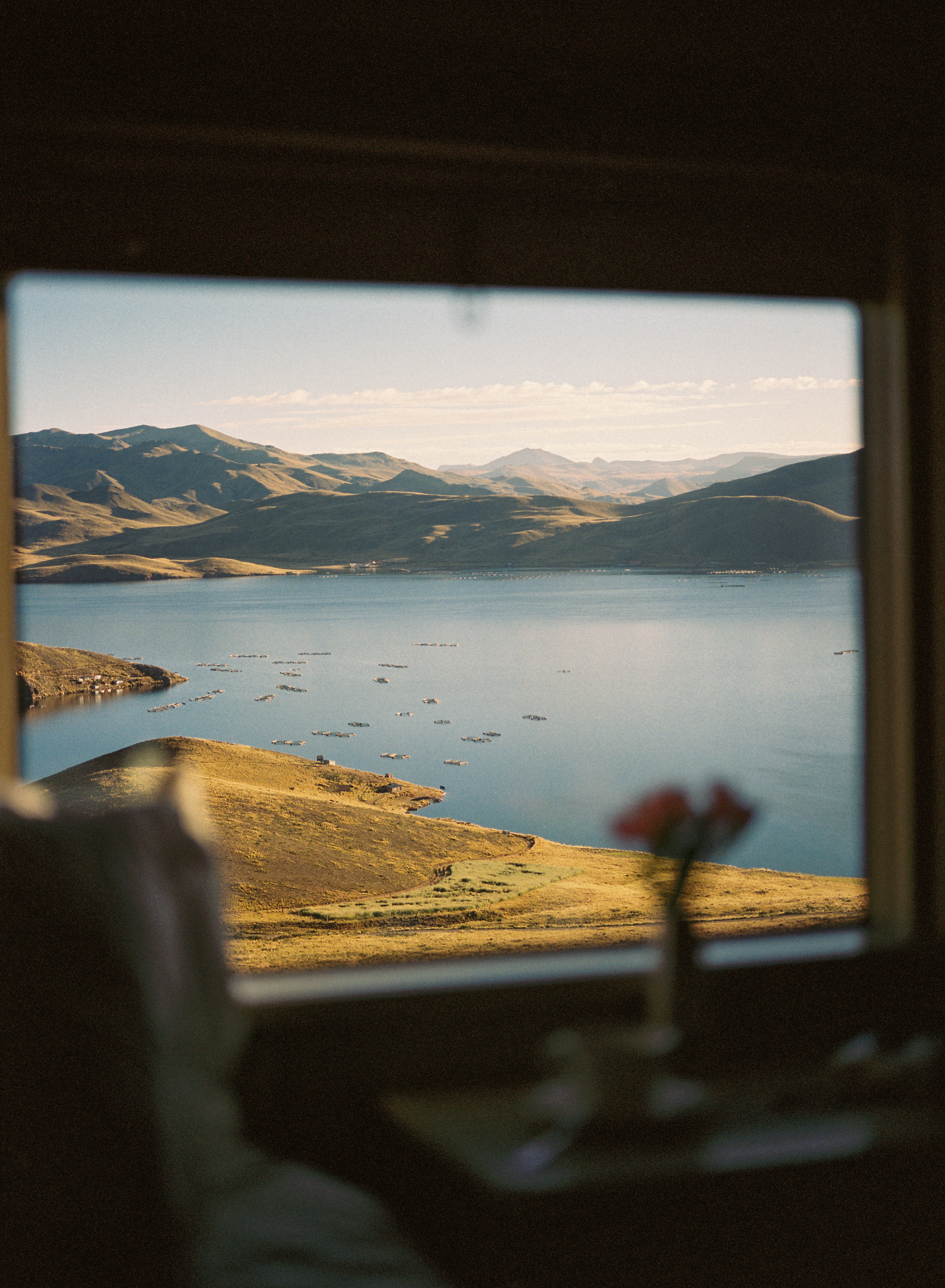 View from a train cabin shows a drink by the window, with lakes and mountains blurred beyond in soft focus.