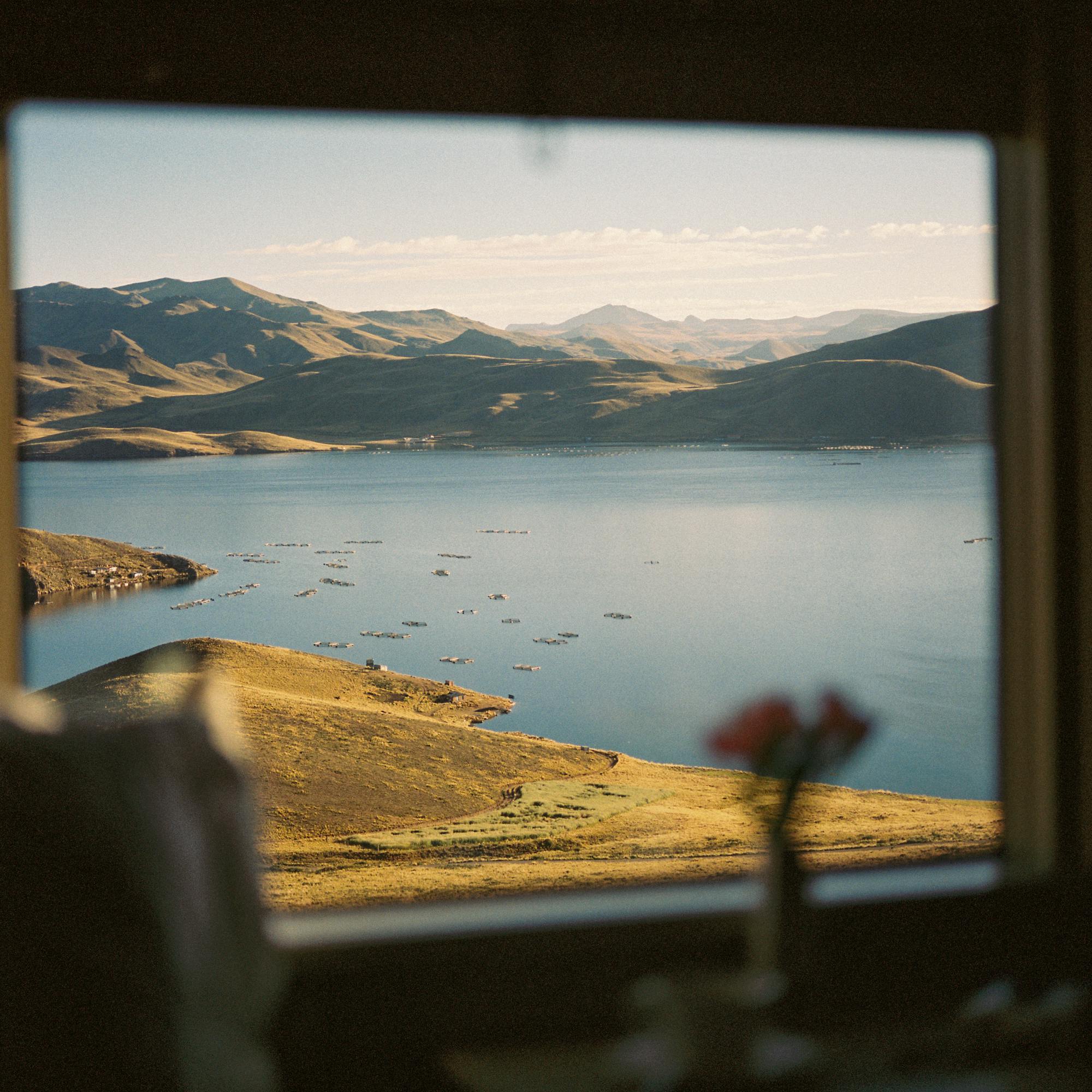 View from a train cabin shows a drink by the window, with lakes and mountains blurred beyond in soft focus.