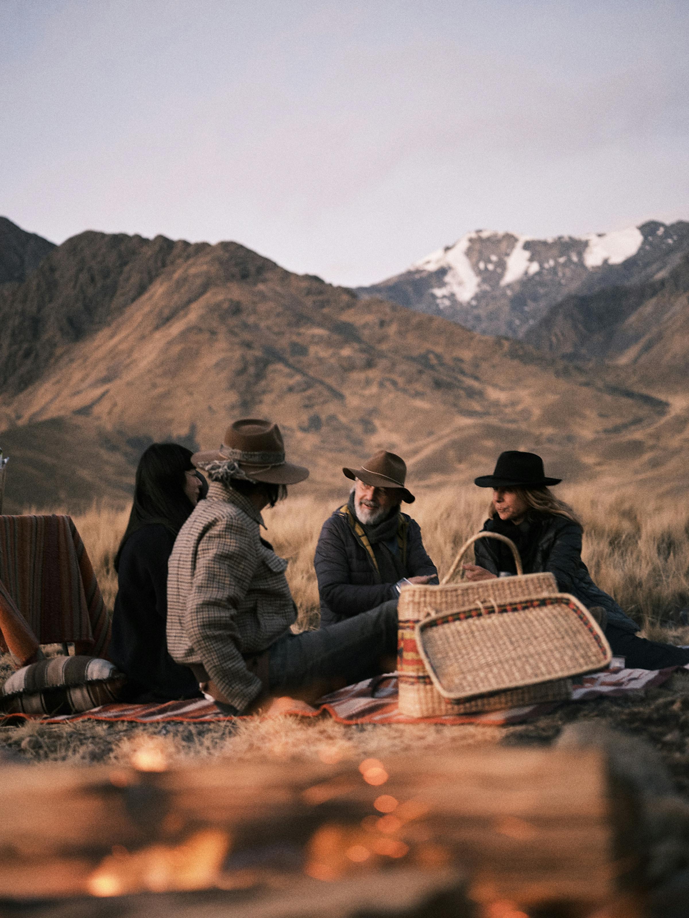 A small group sits on rocks by a highland lake, watching warm sunset light on distant mountains in quiet stillness.