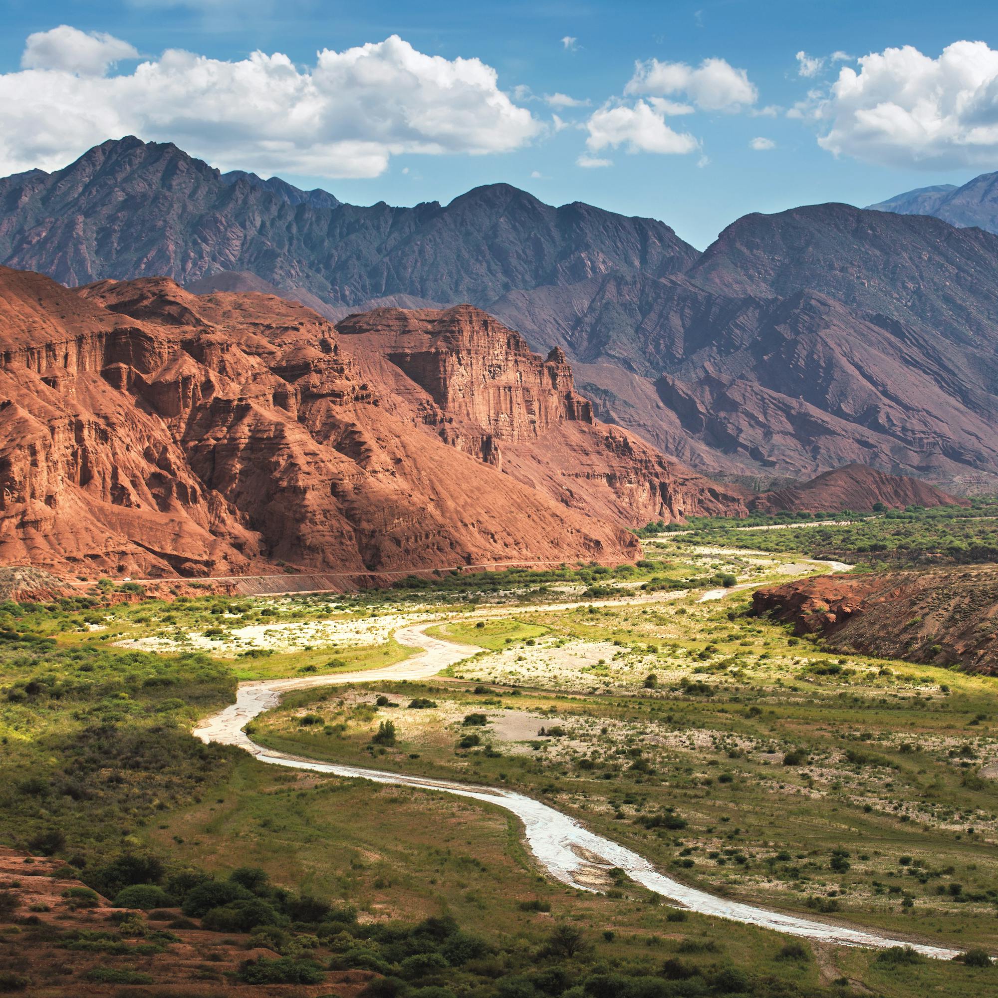 Winding river cuts through a broad red canyon, with layered mountains and blue haze stretching into distance behind it all.