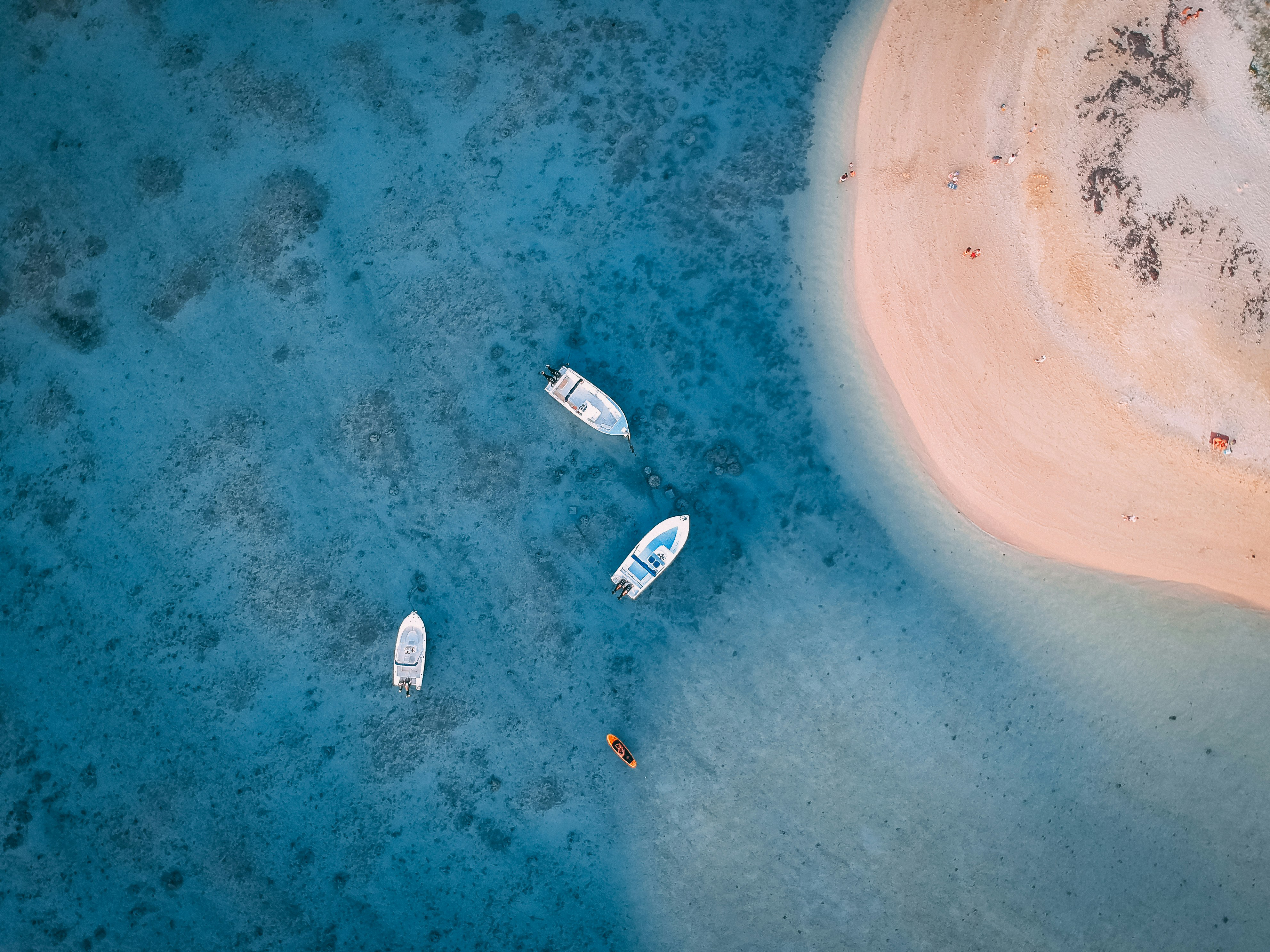 Aerial view of a pale sandbar in blue water, with two small boats anchored nearby and darker reef patches.