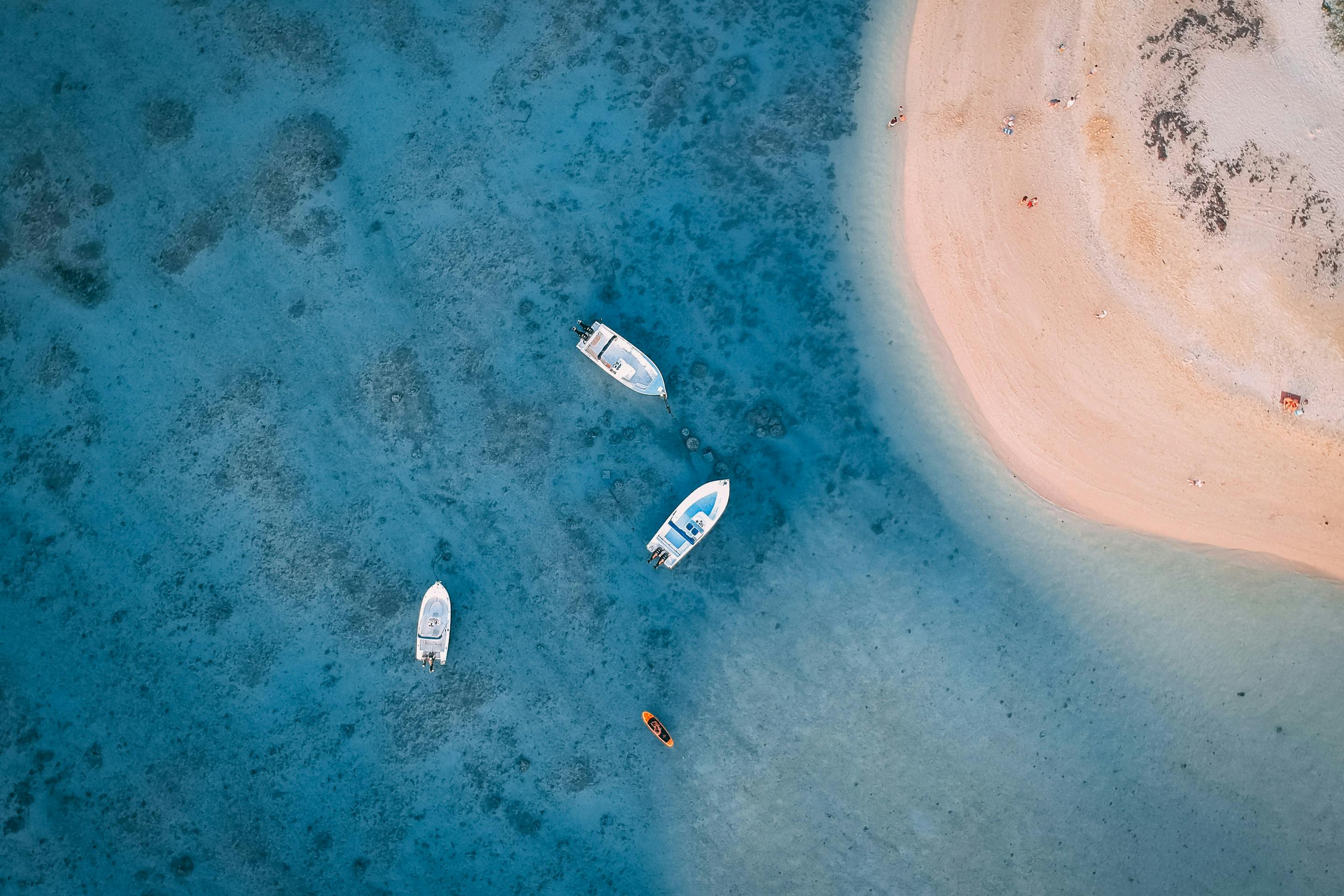 Aerial view of a pale sandbar in blue water, with two small boats anchored nearby and darker reef patches.