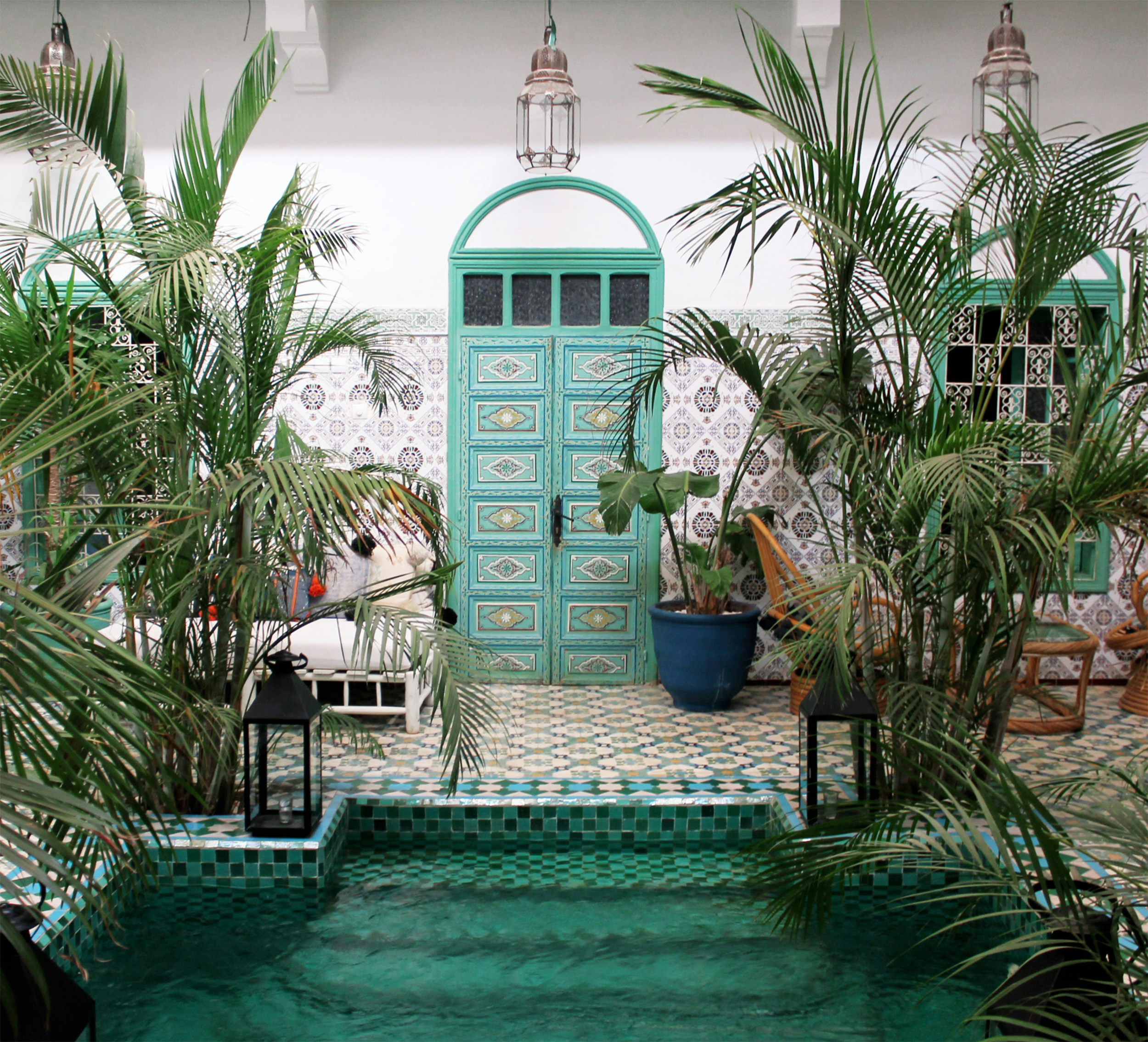 Turquoise door above a small pool surrounded by potted palms and patterned tile.
