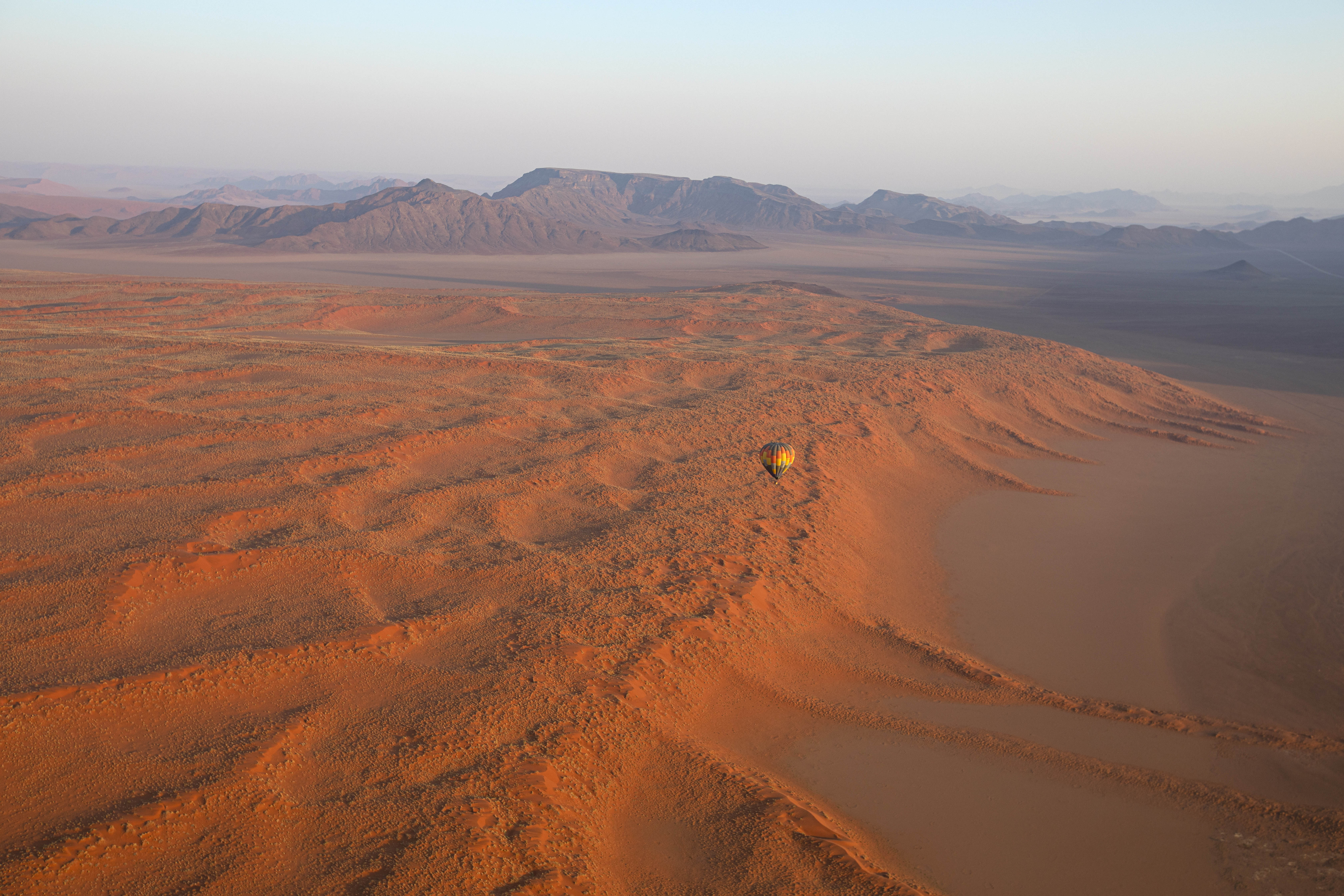 Sunlit dunes ripple across the desert in warm orange tones, with long ridges fading toward the horizon in early light.