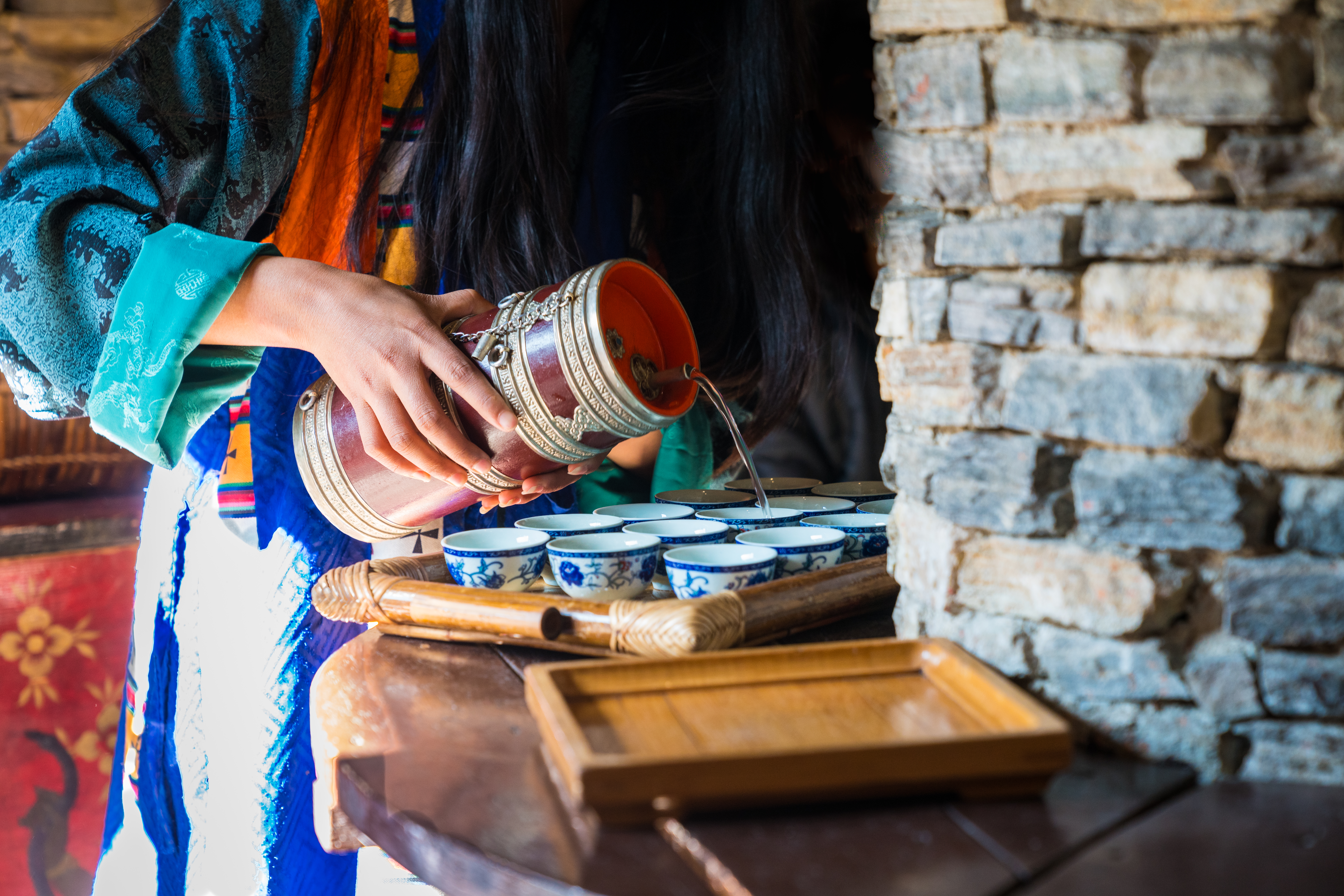 Hands pour tea into small bowls on a table set with cups and dishes.