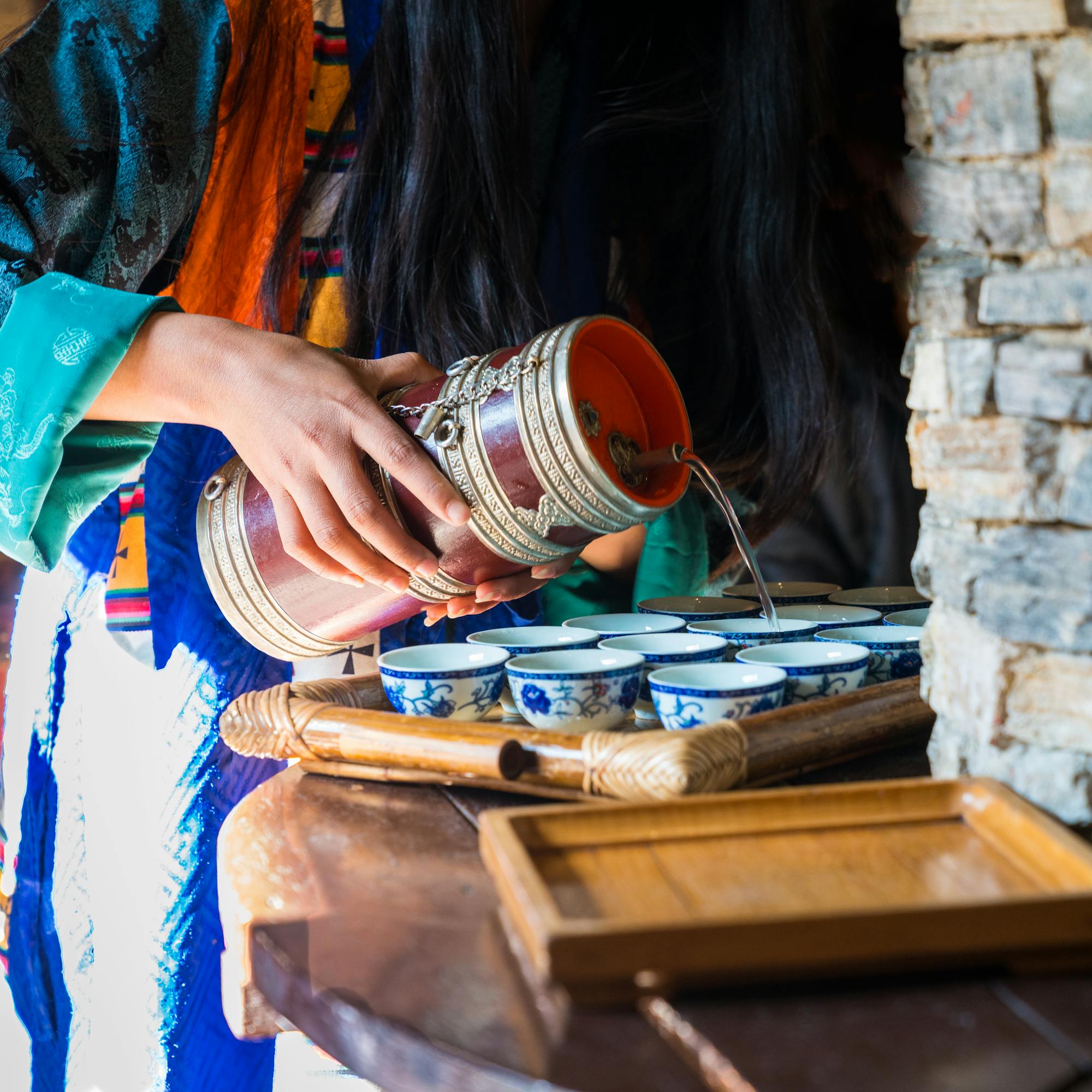 Hands pour tea into small bowls on a table set with cups and dishes.