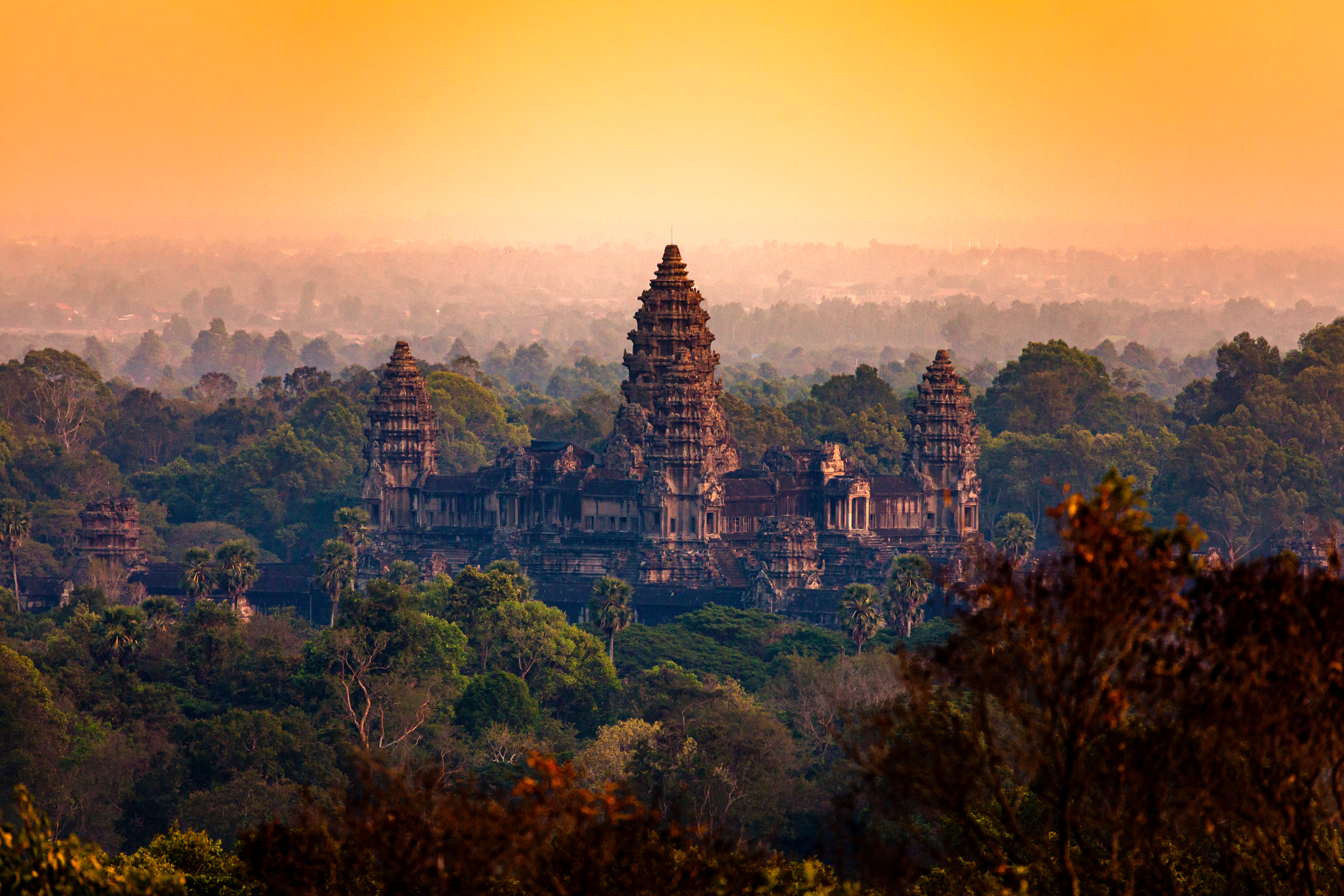 Sunrise light glows over temple towers rising above a forest canopy.