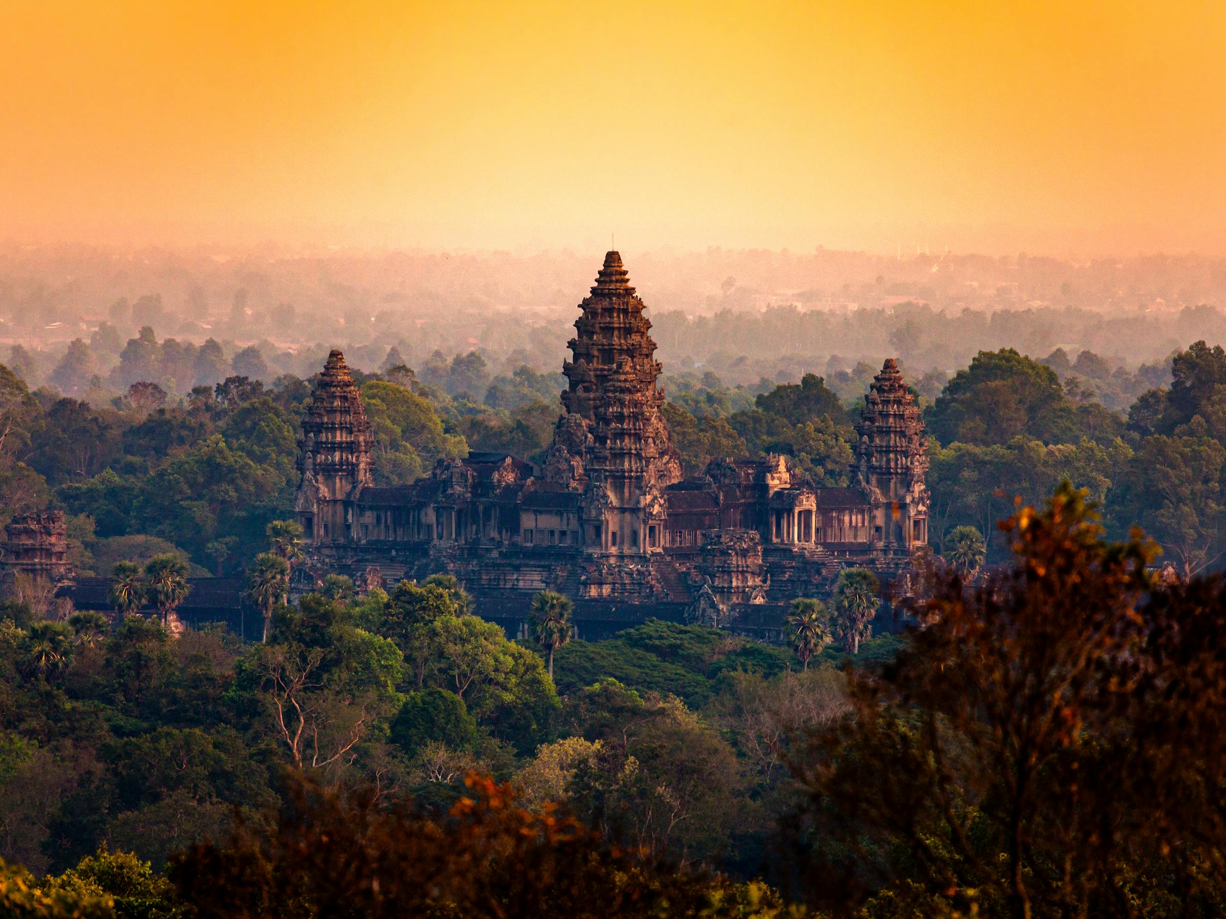 Sunrise light glows over temple towers rising above a forest canopy.