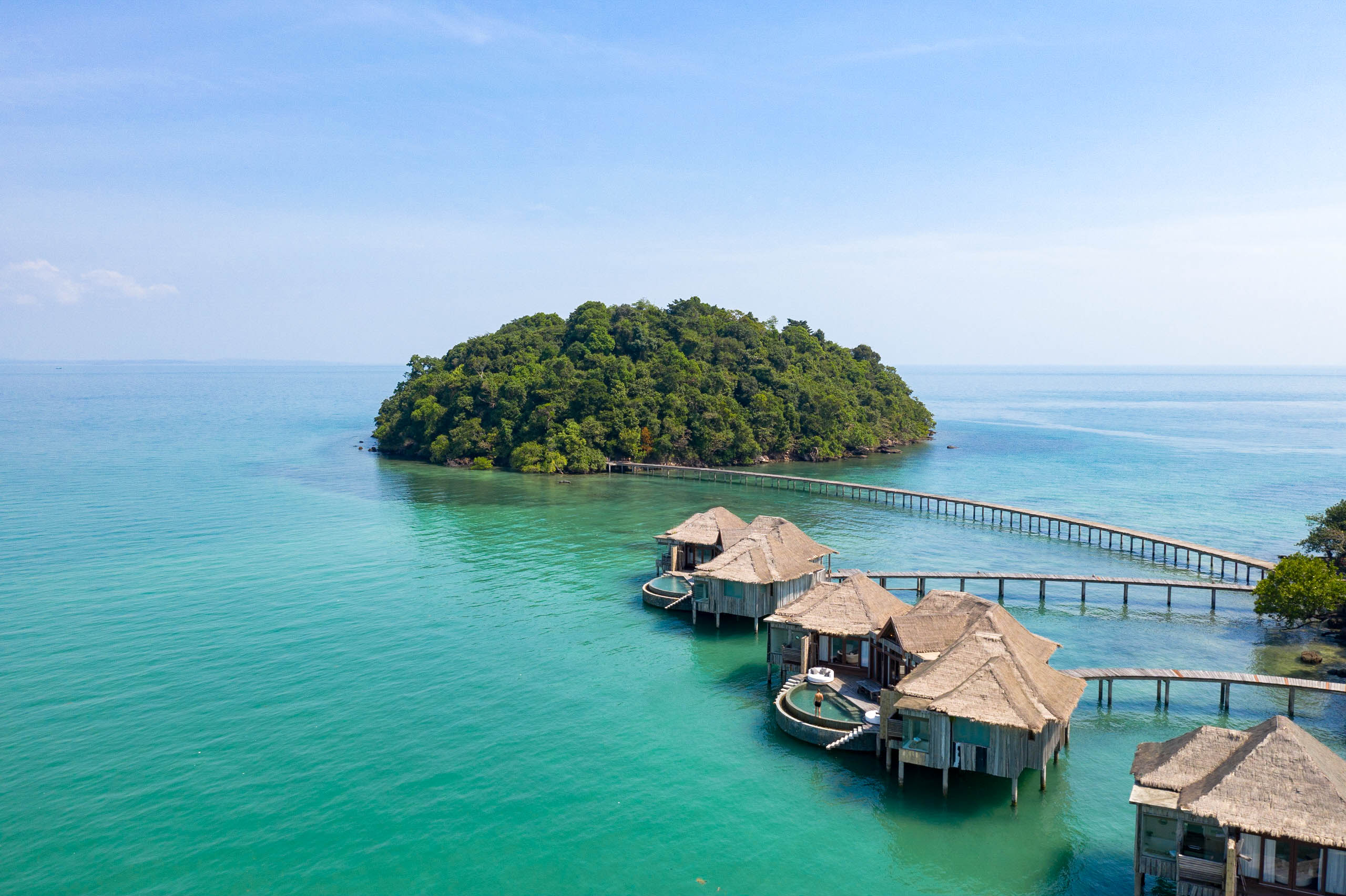 Aerial view of overwater bungalows connected by a pier to a small green island.