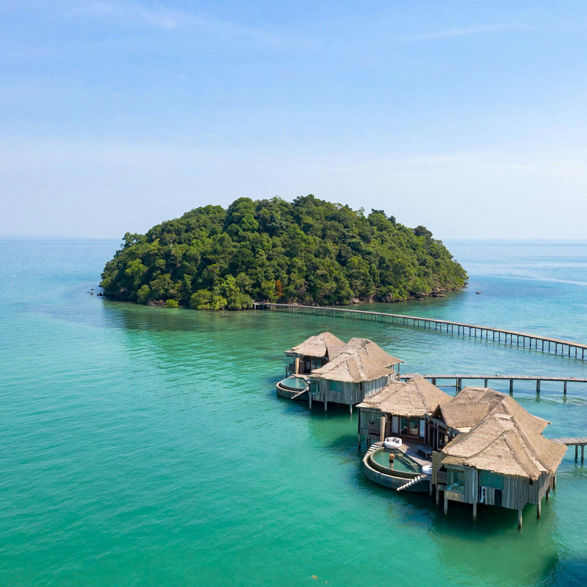 Aerial view of overwater bungalows connected by a pier to a small green island.