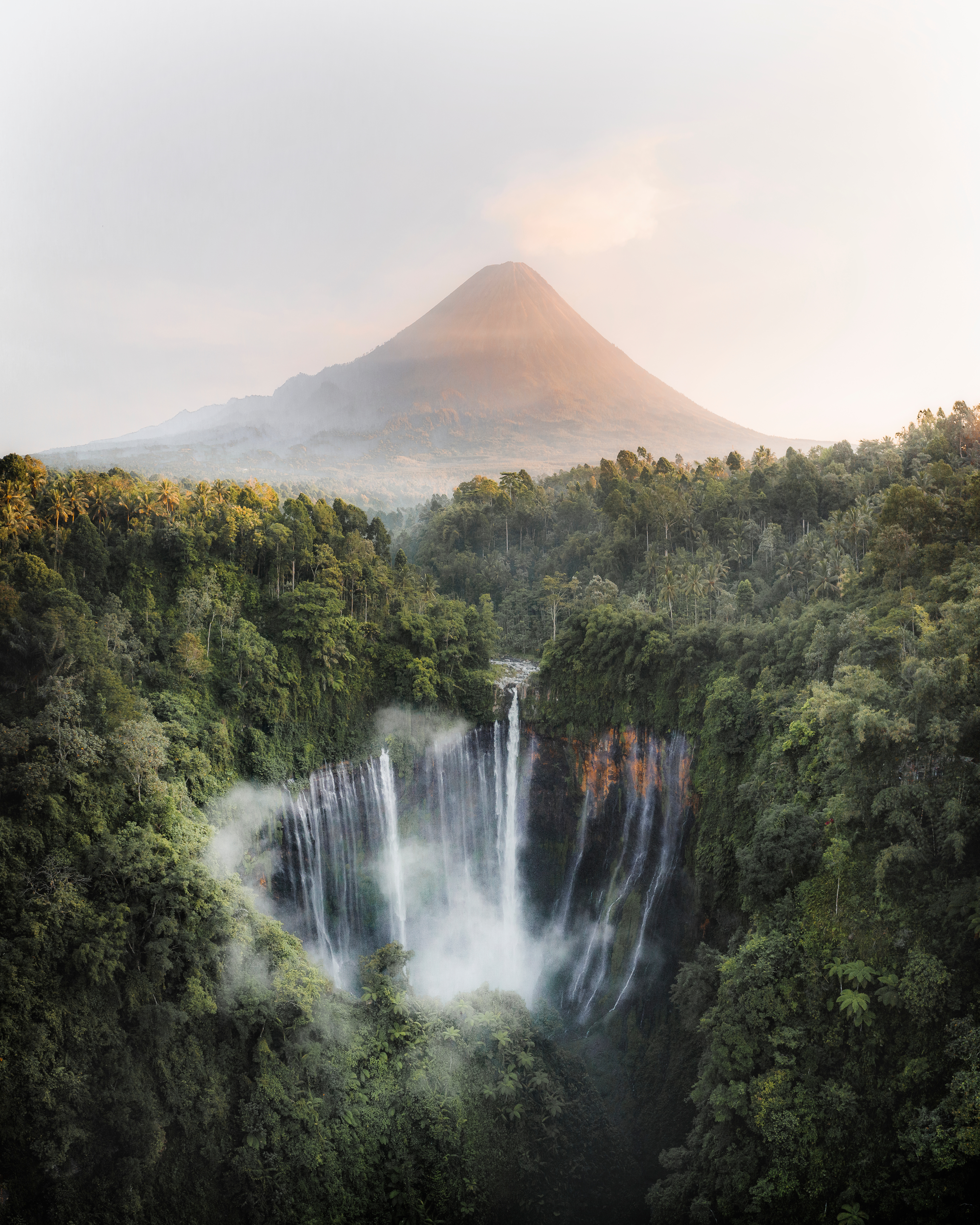 Waterfall cascades through dense jungle with a misty mountain in the background.