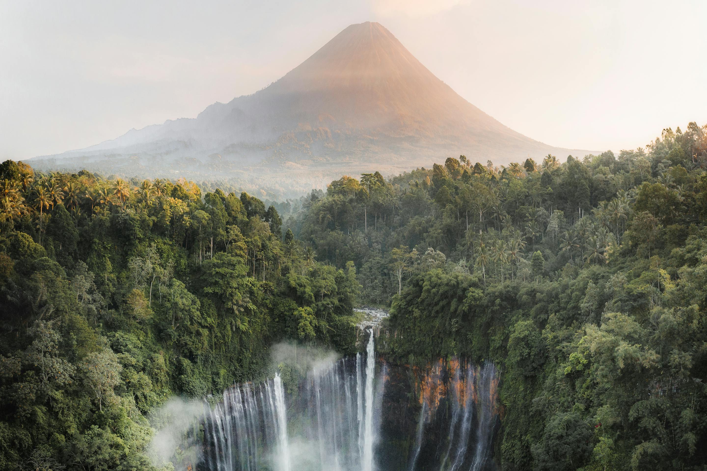 Waterfall cascades through dense jungle with a misty mountain in the background.