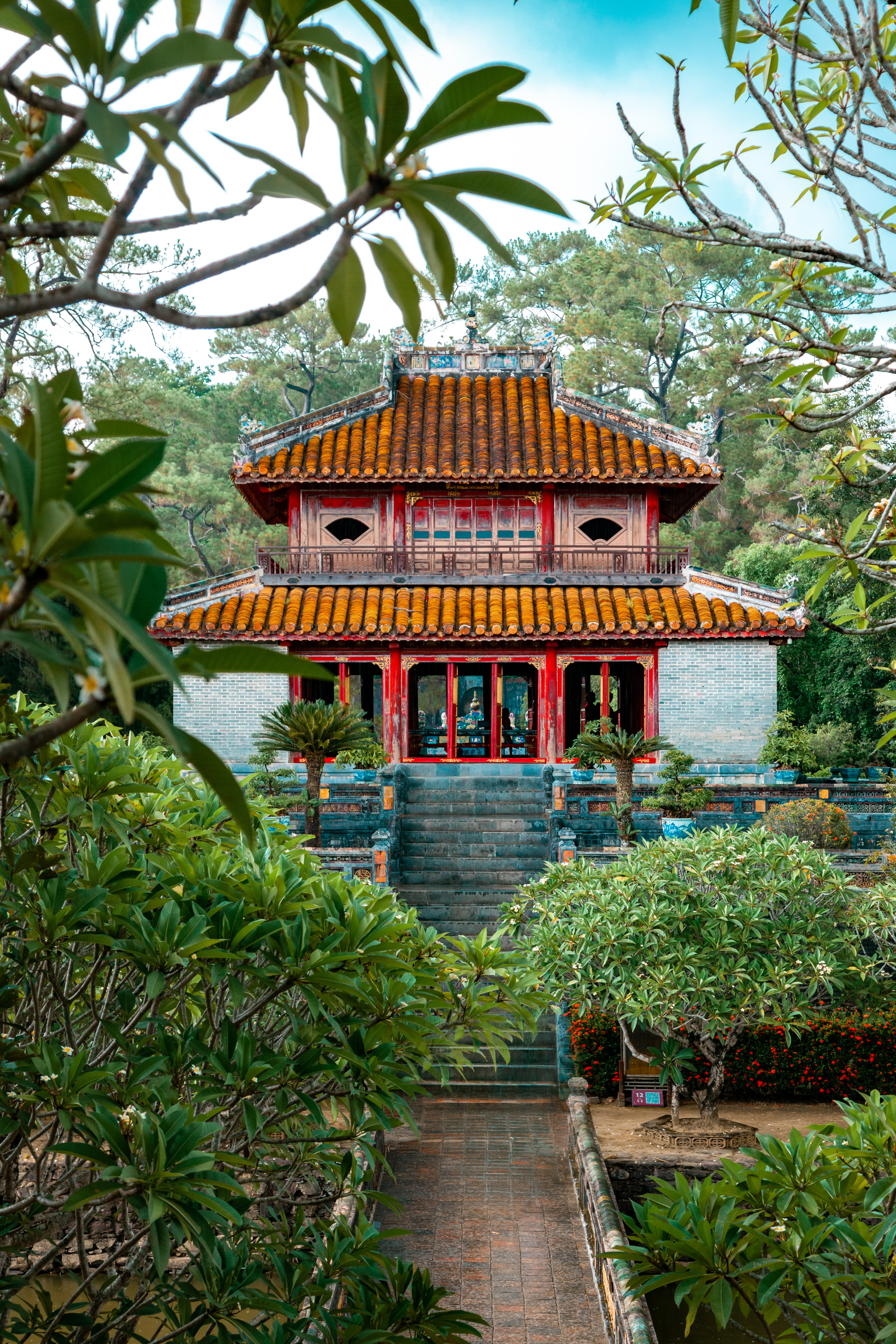 Small temple building sits at the end of a stone path framed by trees and shrubs.