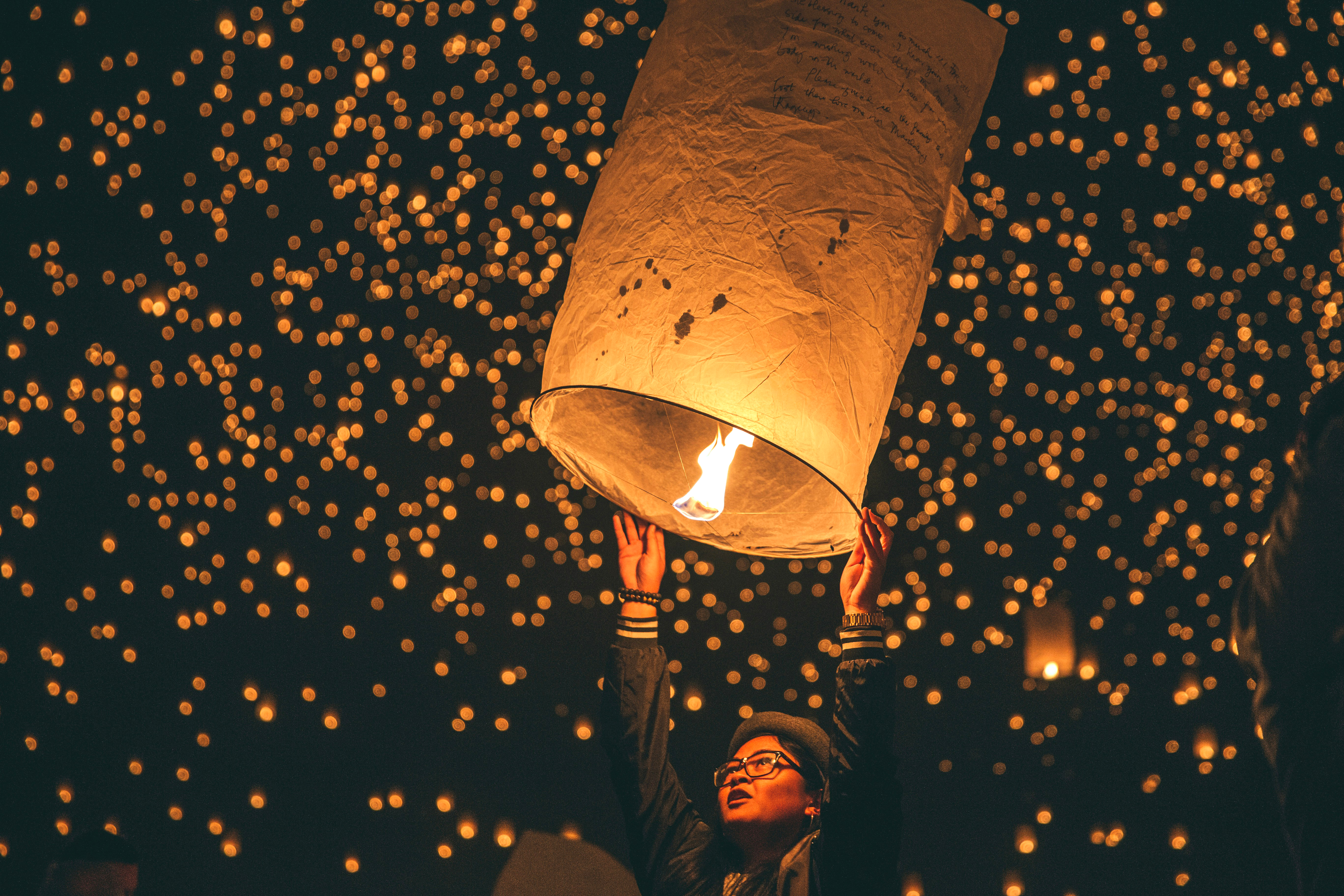 Person releases a paper lantern as glowing lanterns fill the night sky.