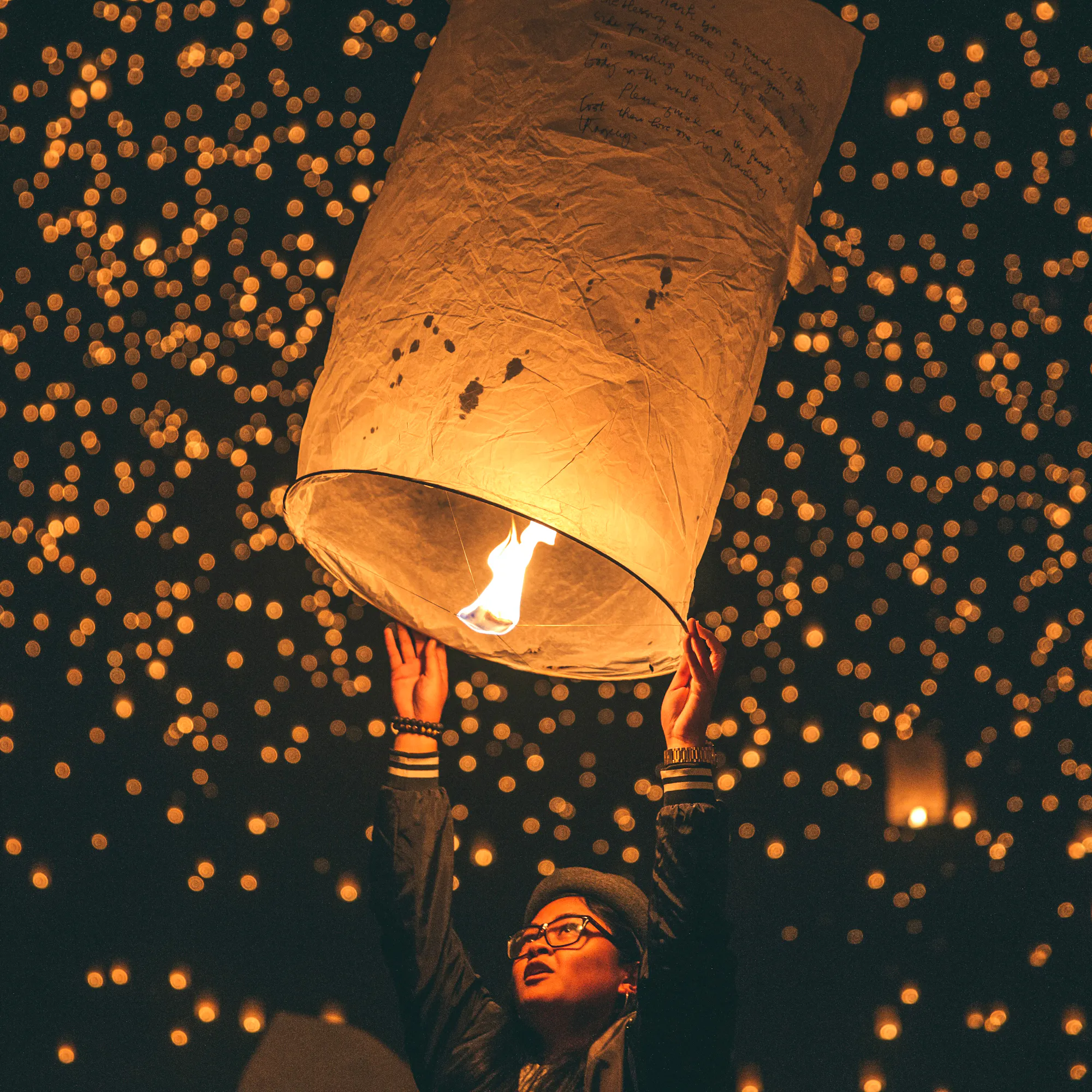 Person releases a paper lantern as glowing lanterns fill the night sky.