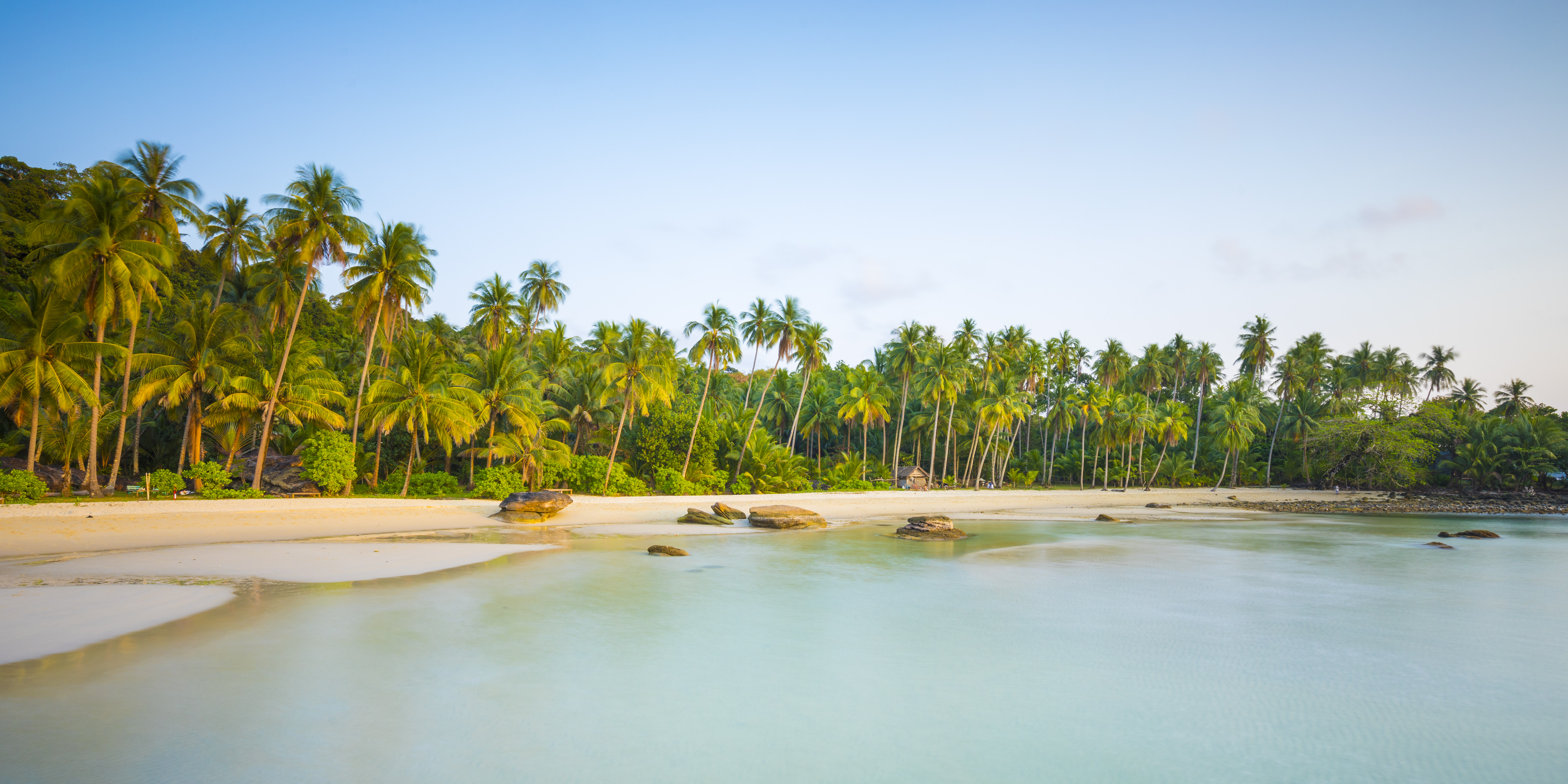 Palm trees line a calm tropical lagoon with pale sand and clear water.