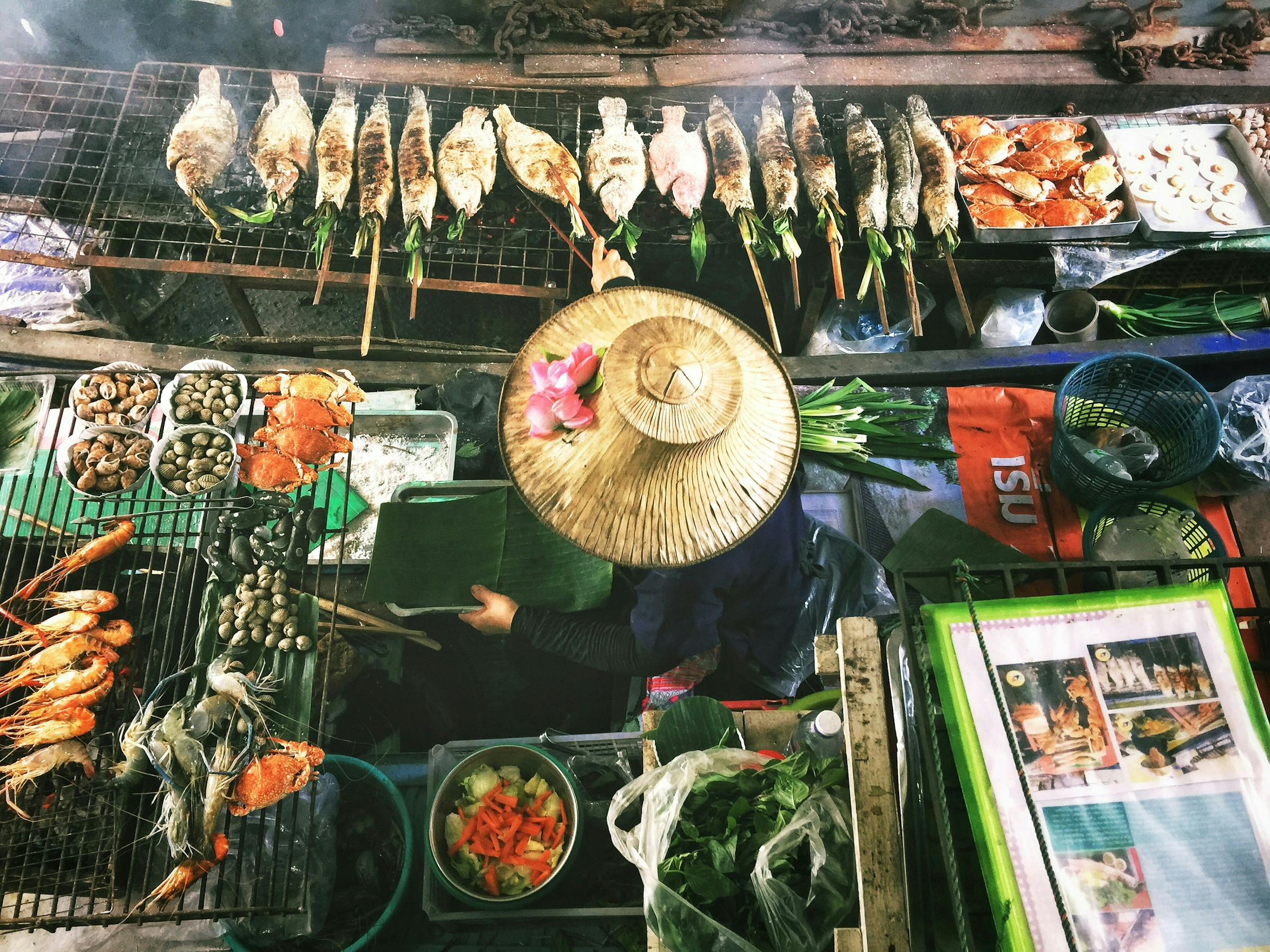 Overhead view of a market stall with seafood, produce, and a conical hat.