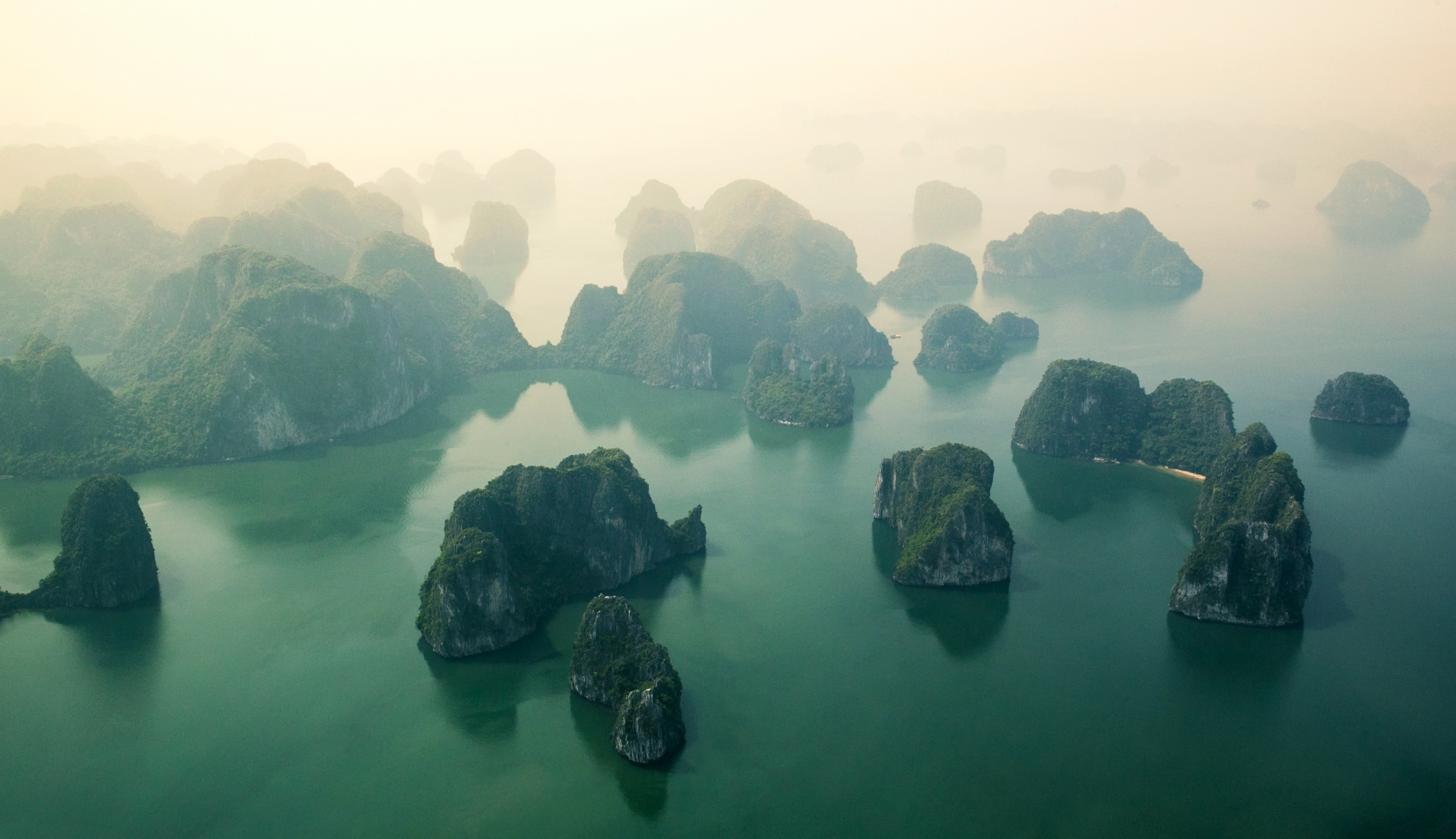 Misty limestone islands rise from green water under a hazy sky.