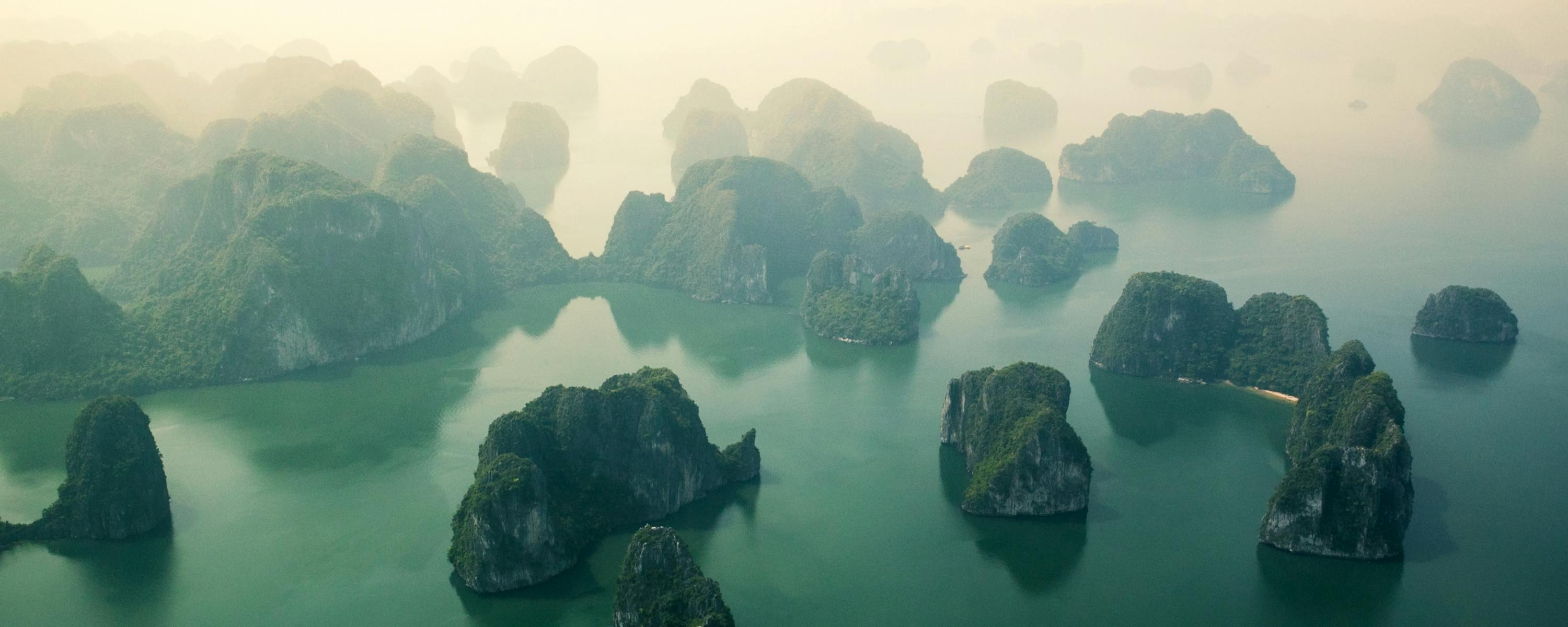 Misty limestone islands rise from green water under a hazy sky.