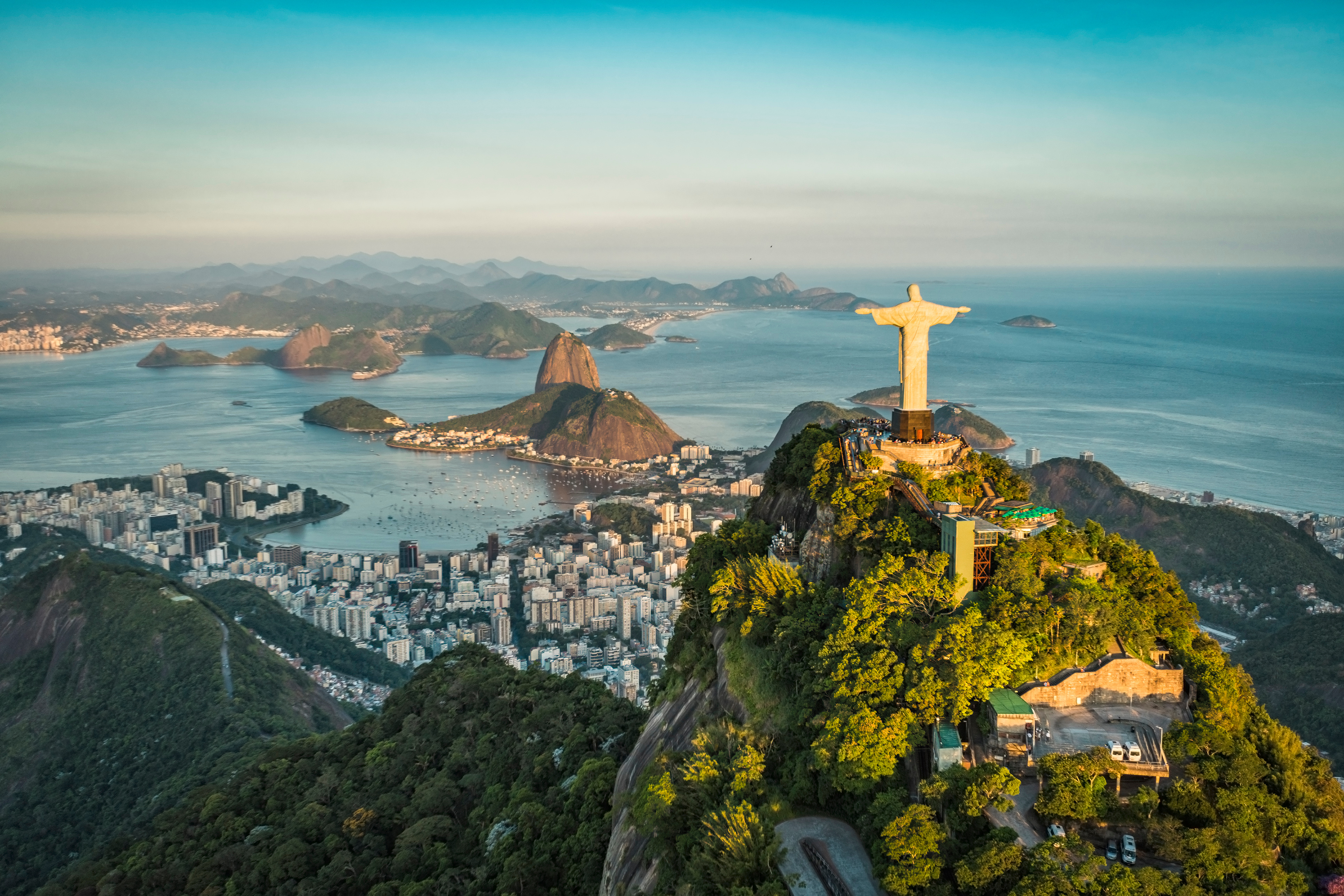 Aerial view of a hilltop statue overlooking a coastal city and blue bay.