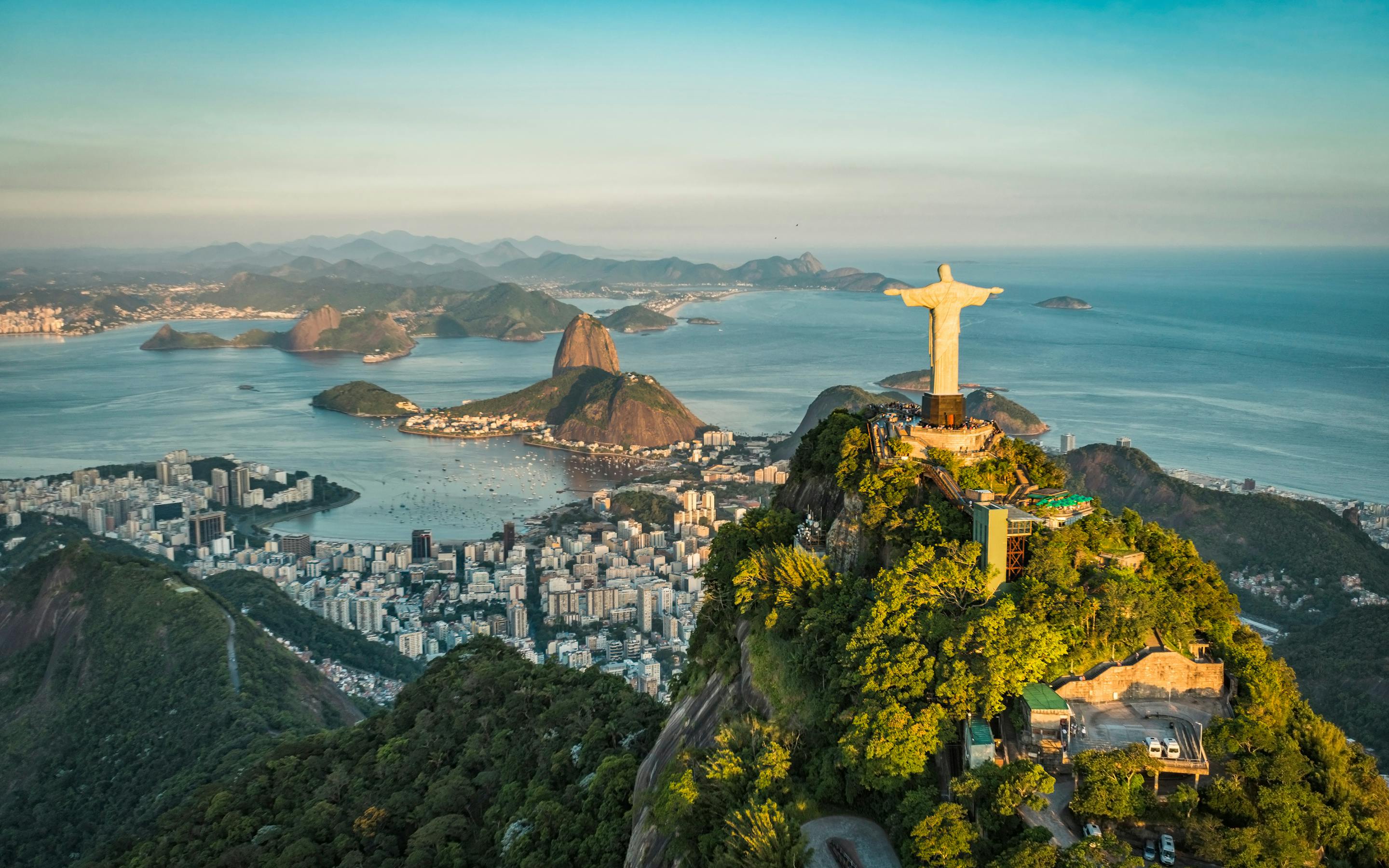 Aerial view of a hilltop statue overlooking a coastal city and blue bay.