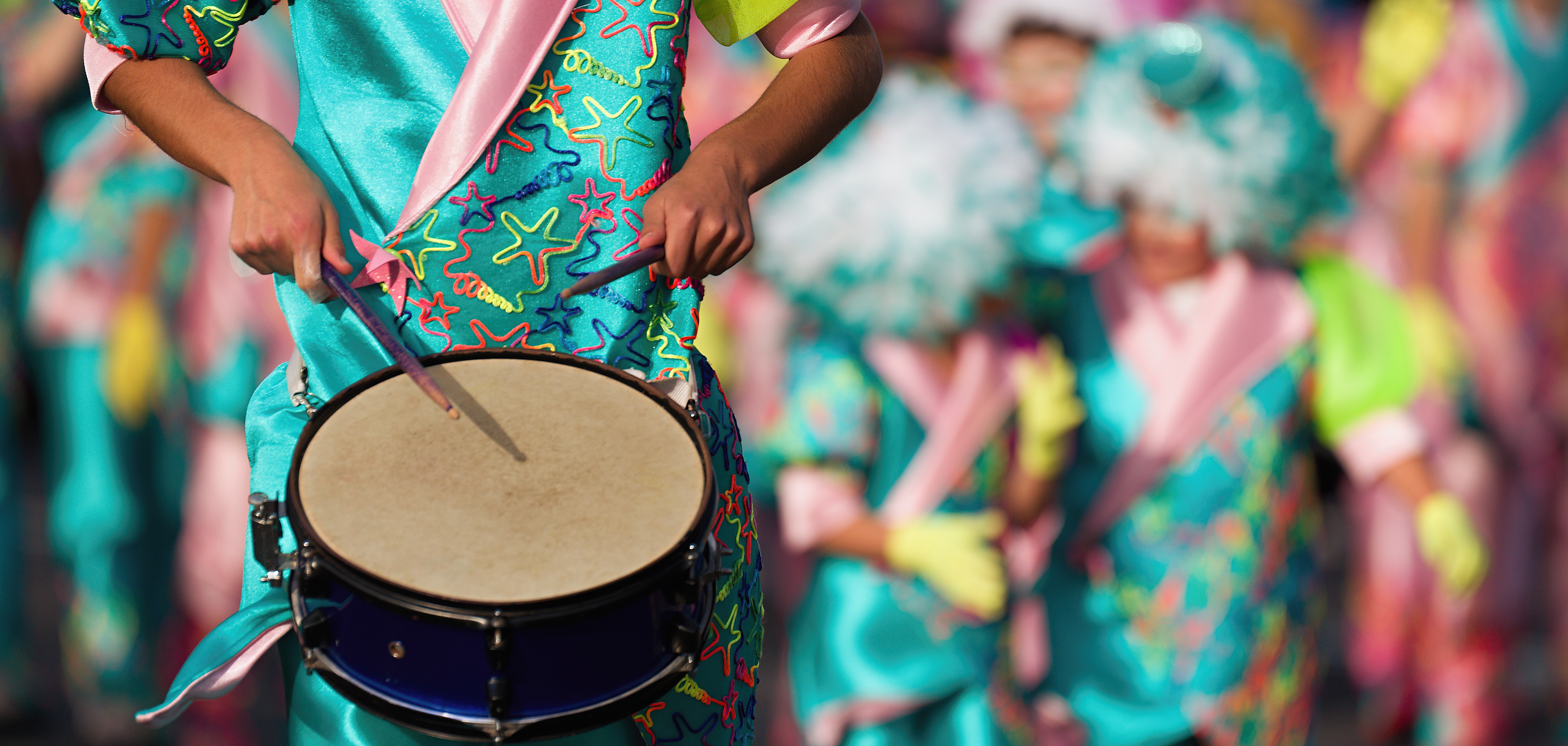 Close-up of hands playing a drum during a colorful street parade.