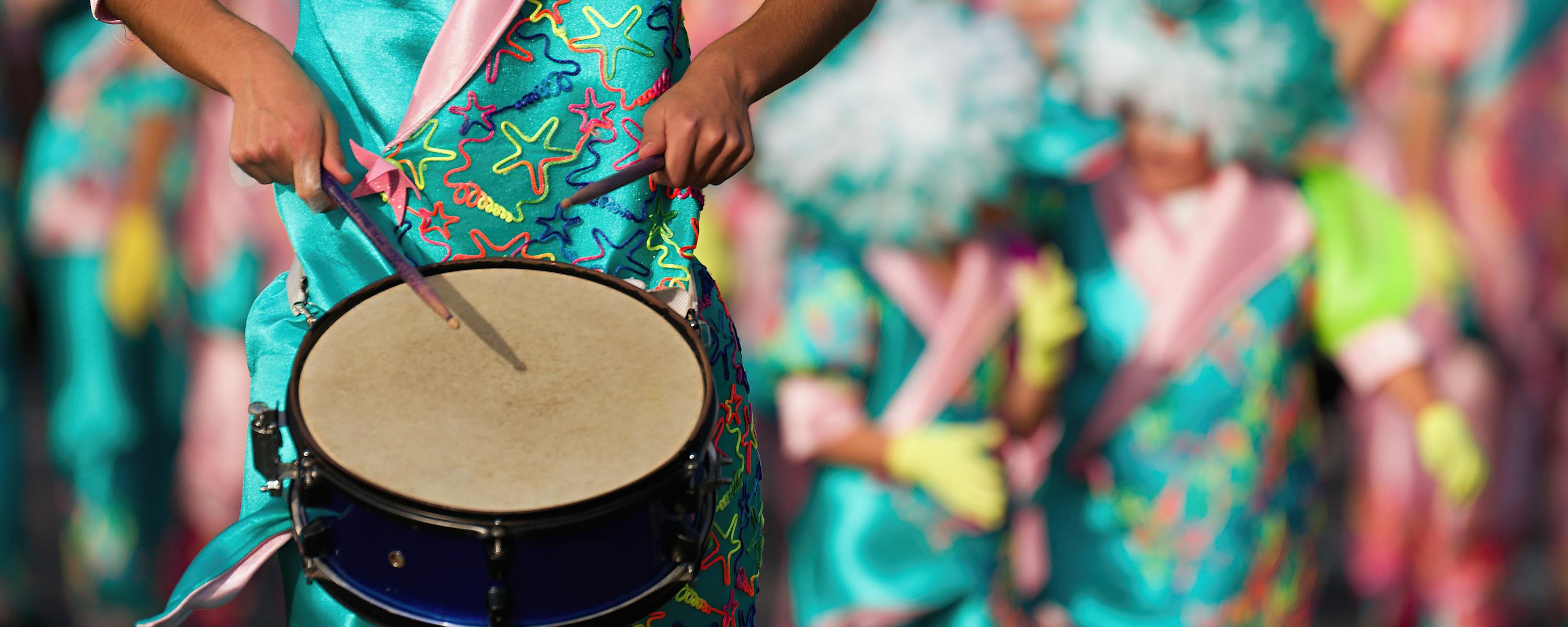 Close-up of hands playing a drum during a colorful street parade.