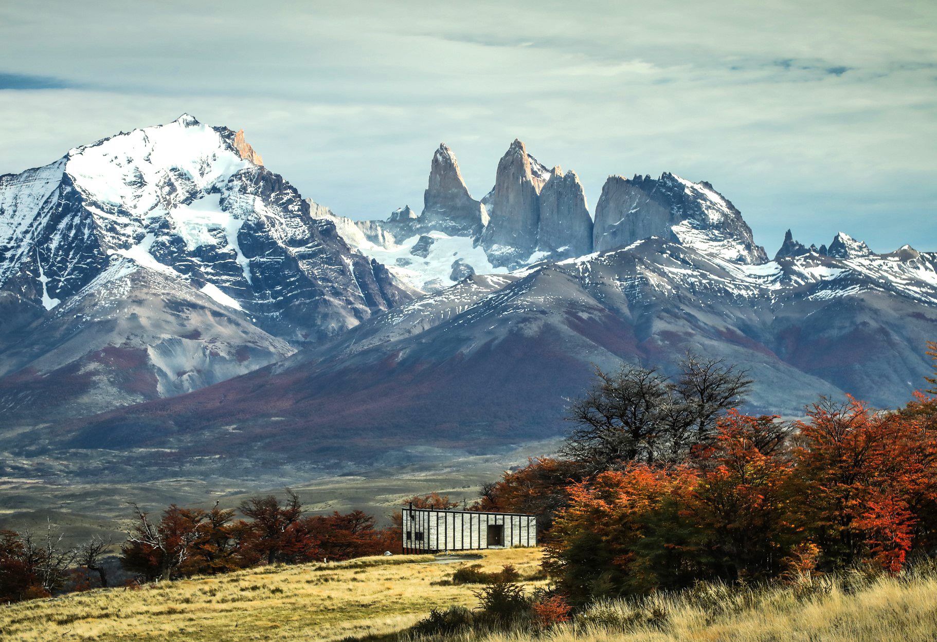 Mountain peaks rise behind a small lodge building with autumn trees in the foreground.