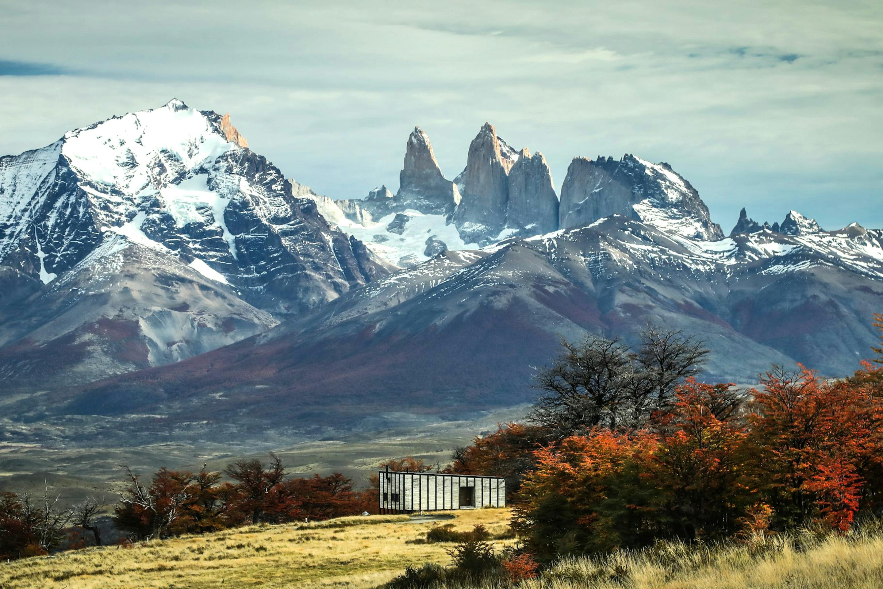 Mountain peaks rise behind a small lodge building with autumn trees in the foreground.
