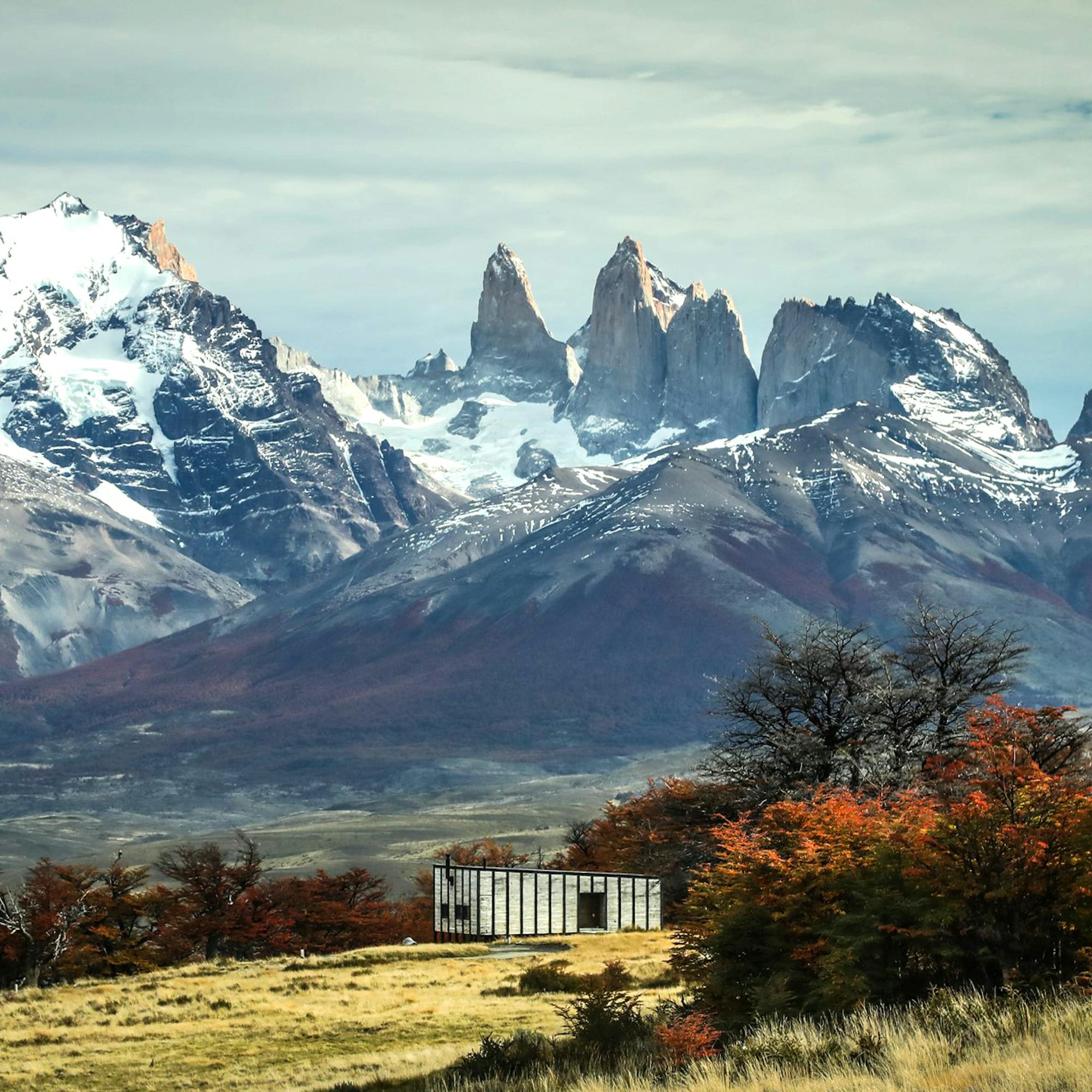 Mountain peaks rise behind a small lodge building with autumn trees in the foreground.