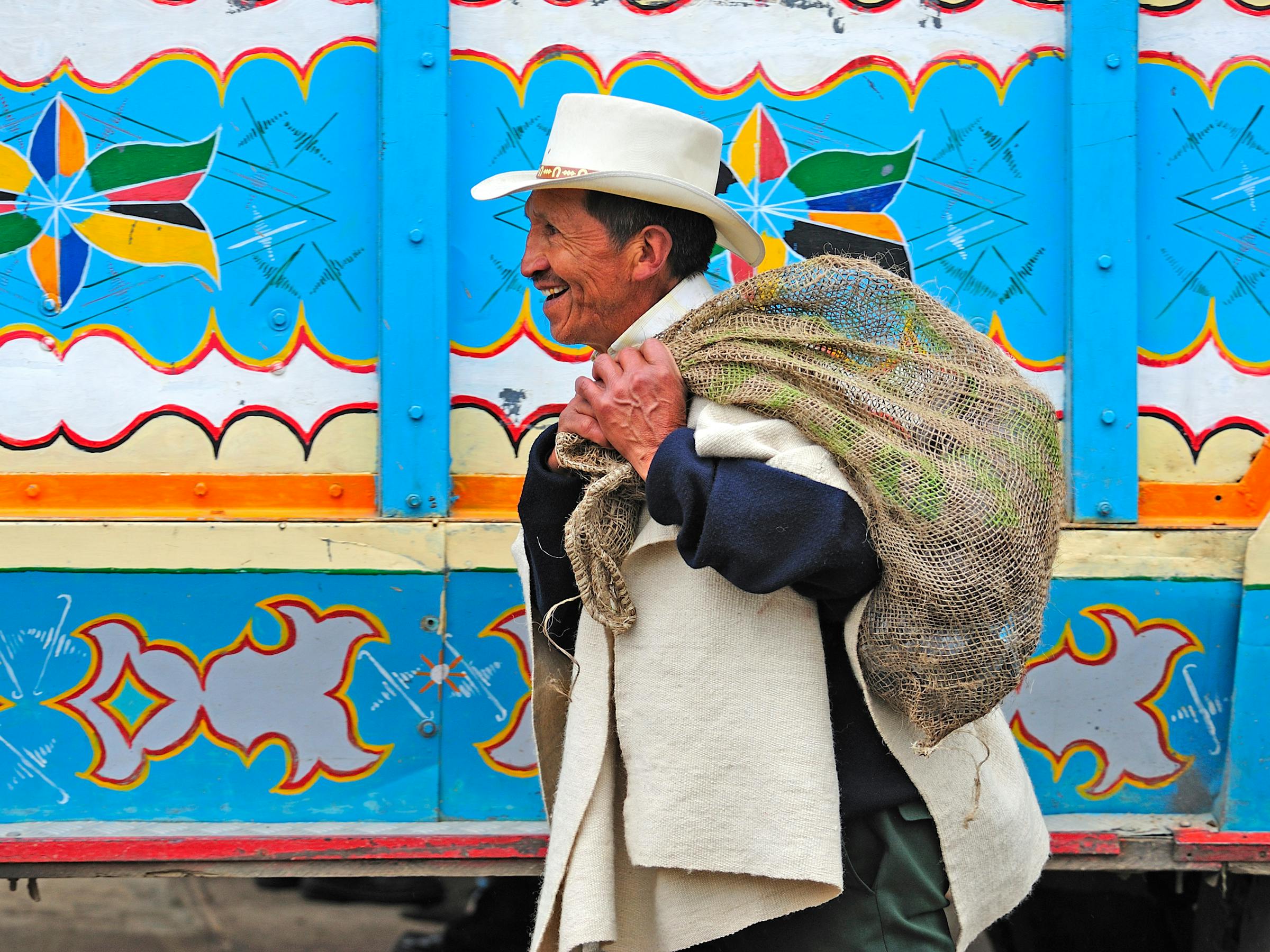 Man in a hat carries a bundle past a brightly painted wall with colorful patterns.