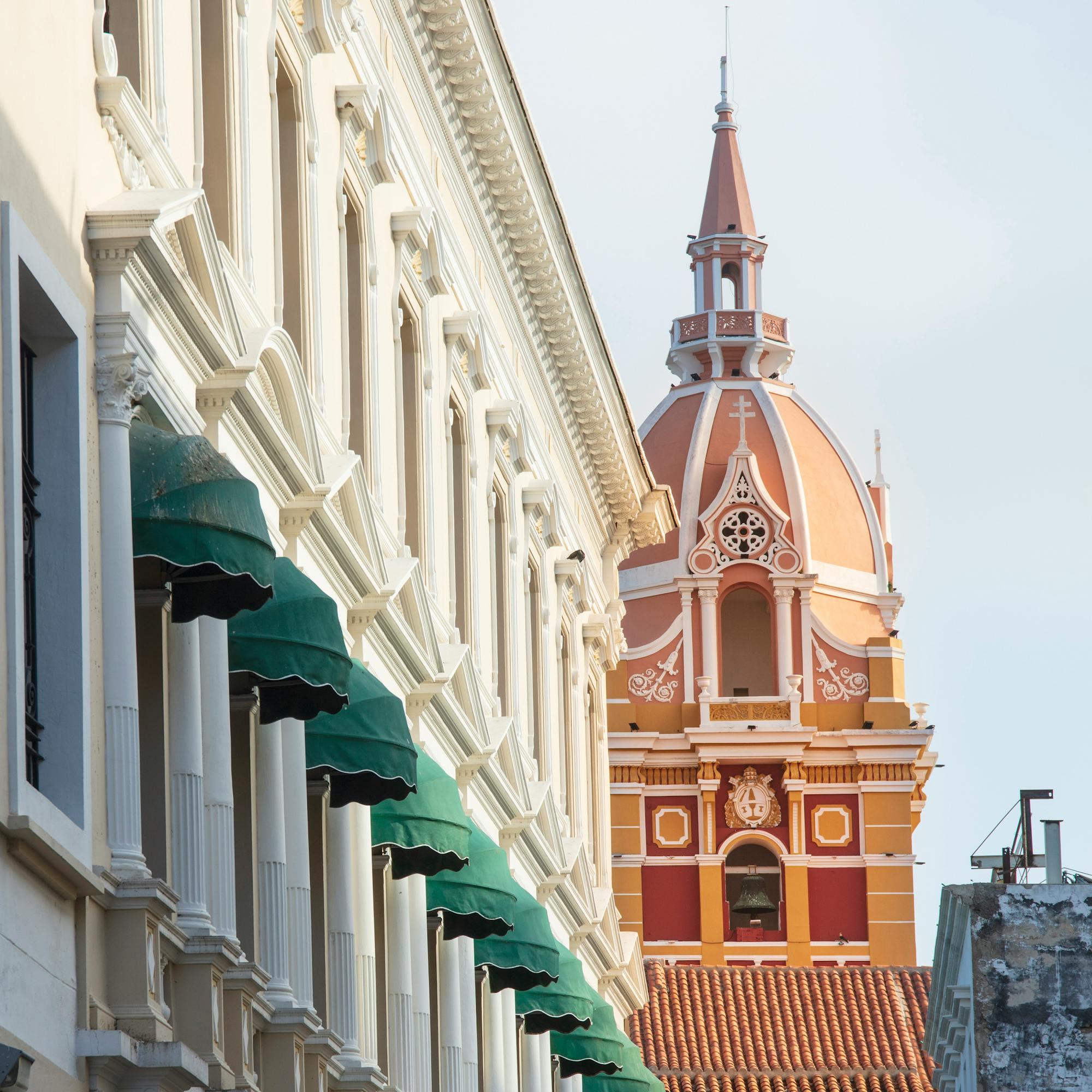 Orange church tower rises at the end of a street framed by white buildings and green awnings.
