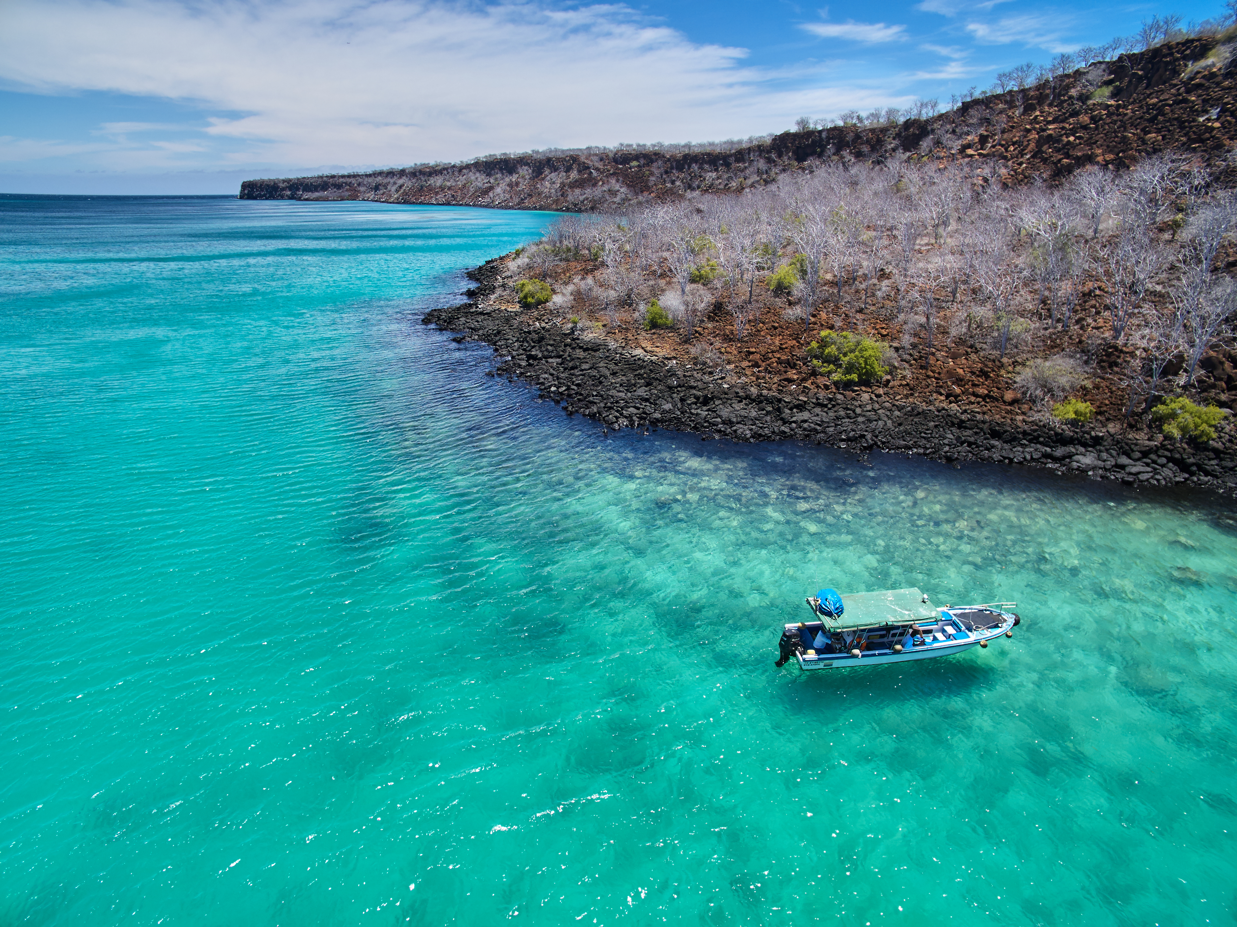 Small boat floats in turquoise water beside a rocky shoreline.