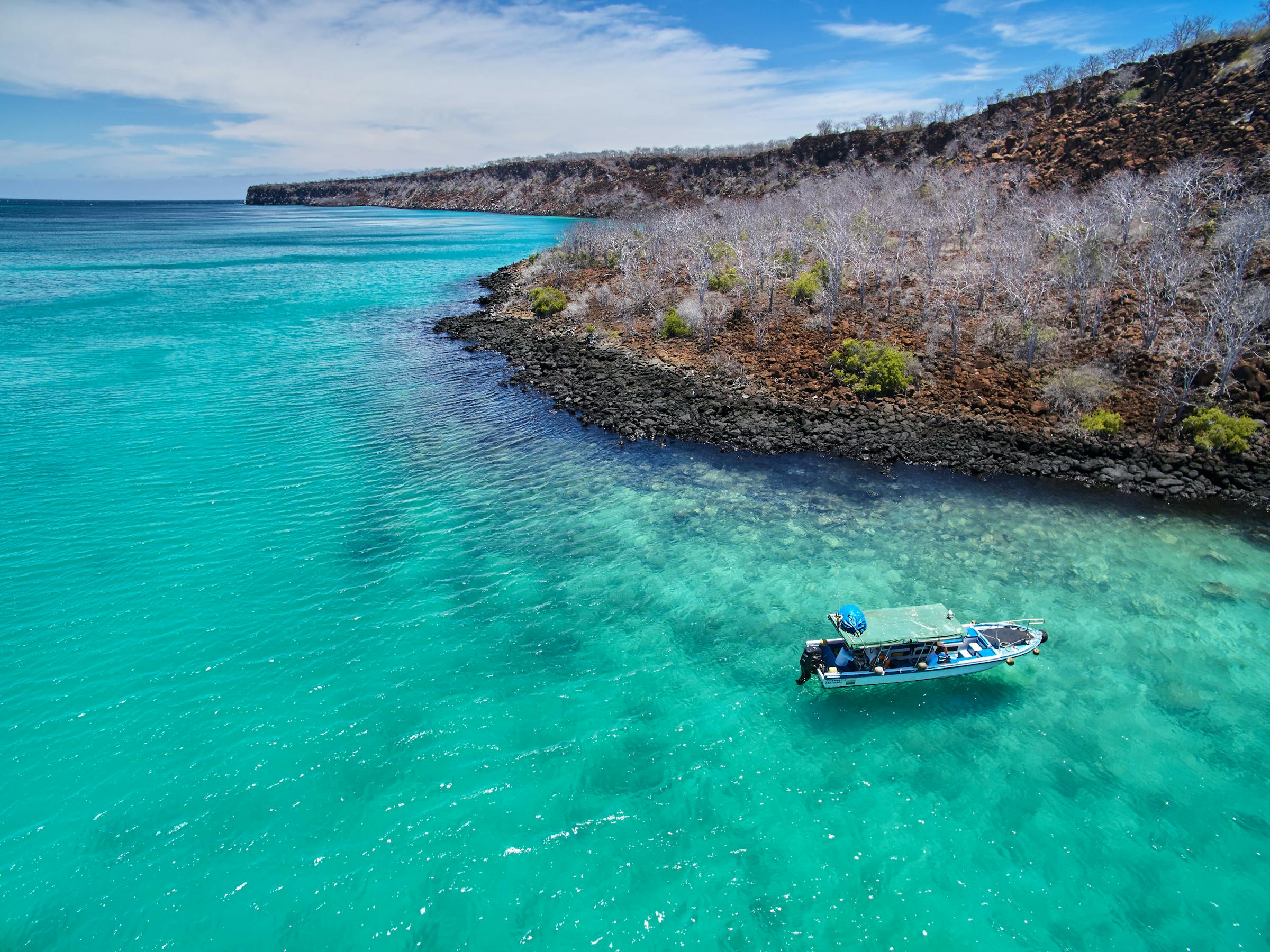 Small boat floats in turquoise water beside a rocky shoreline.