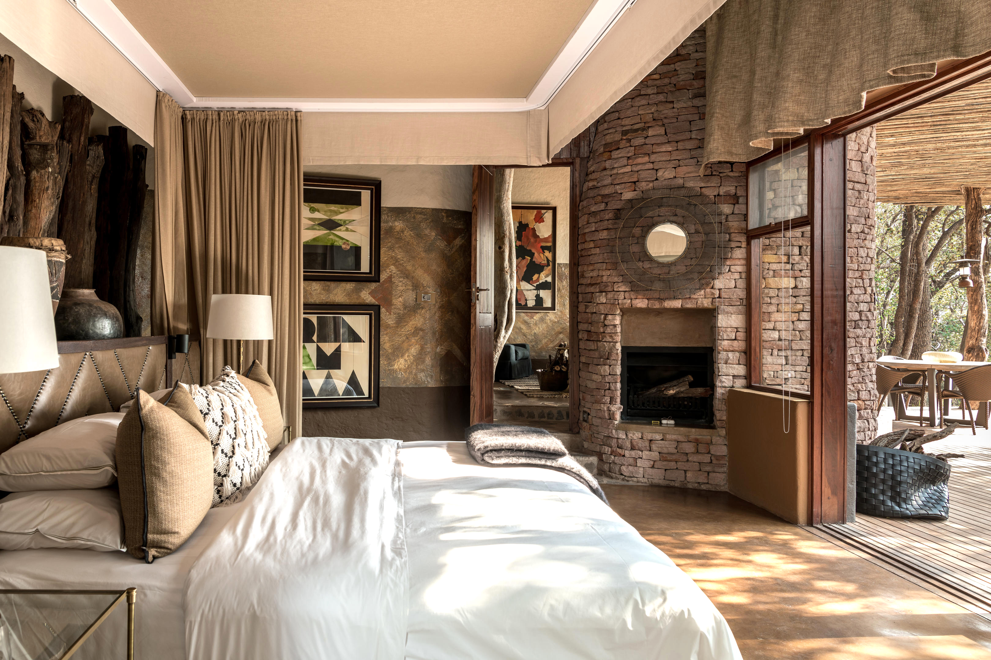 Bright bedroom with white bedding and framed art opens to a terrace, with a brick fireplace beside the door.