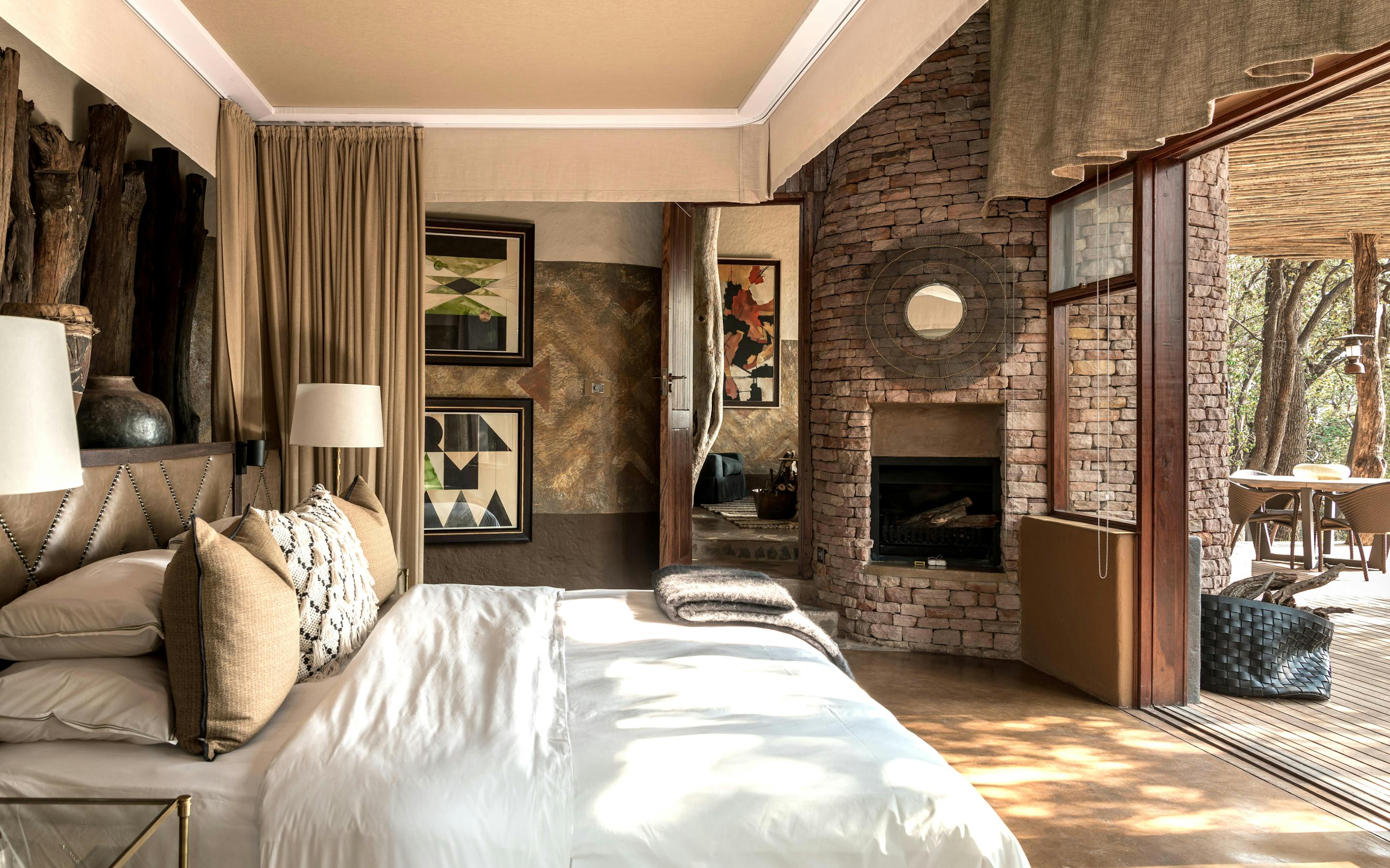 Bright bedroom with white bedding and framed art opens to a terrace, with a brick fireplace beside the door.