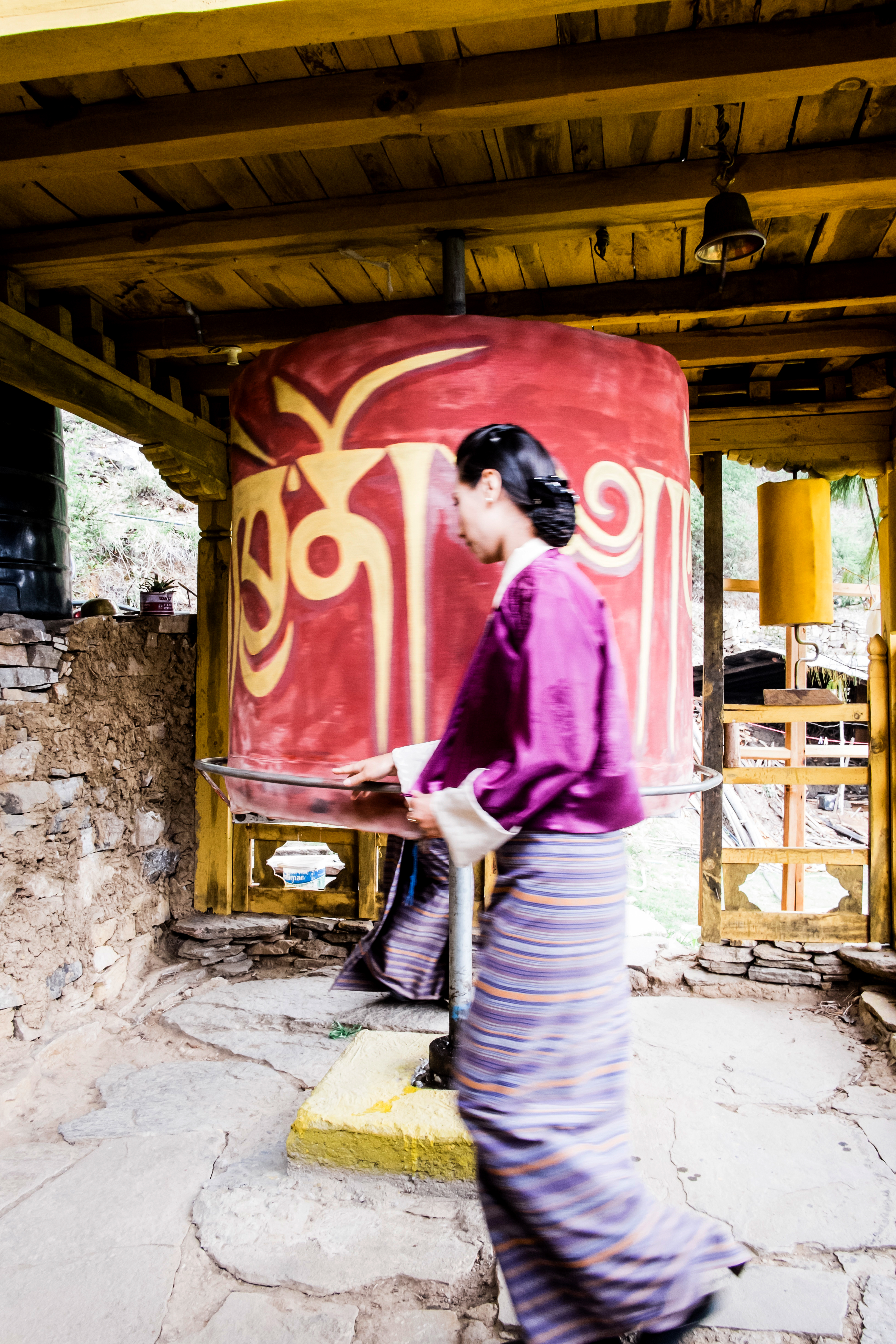 Person spins a large painted wheel under a wooden shelter.
