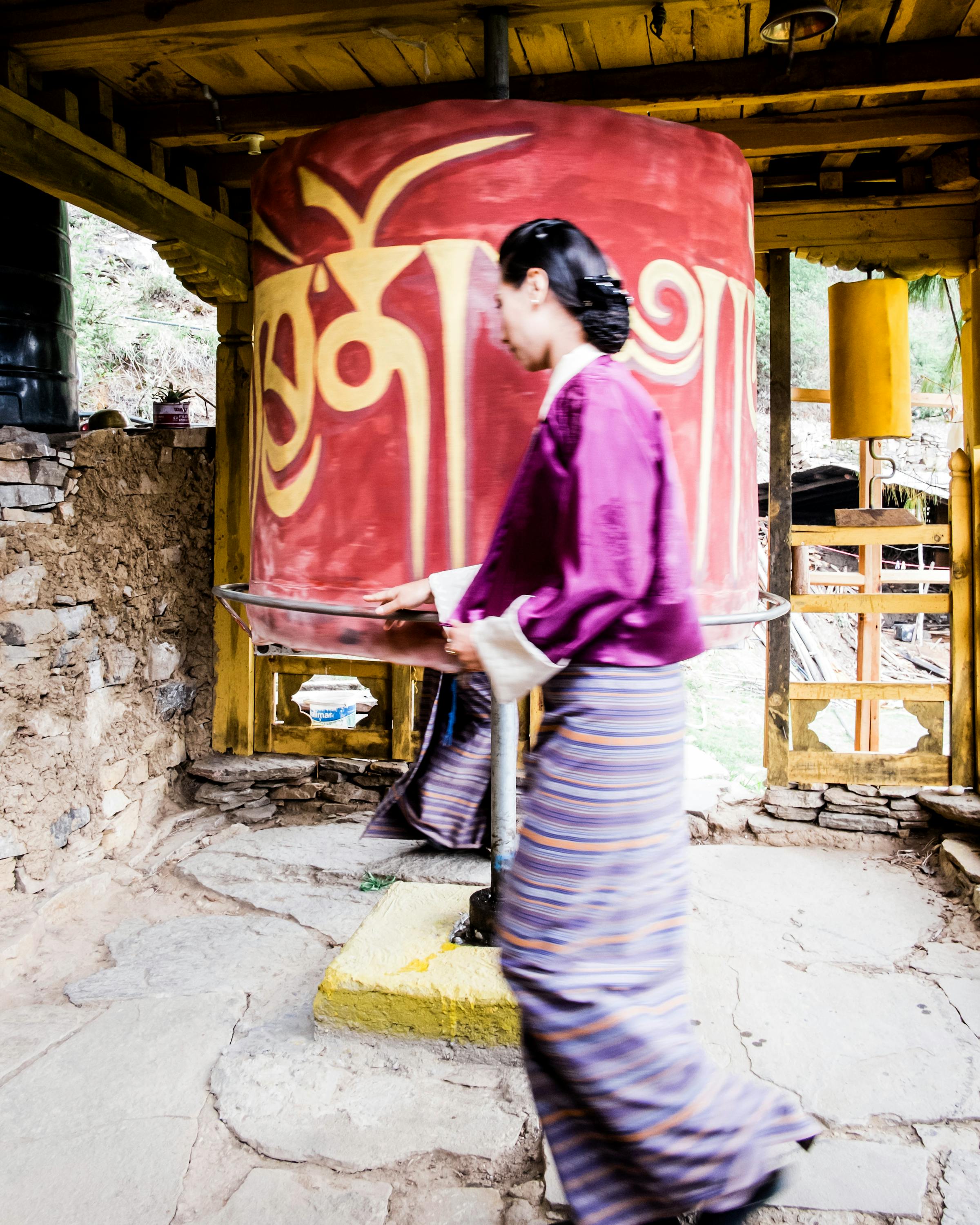 Person spins a large painted wheel under a wooden shelter.