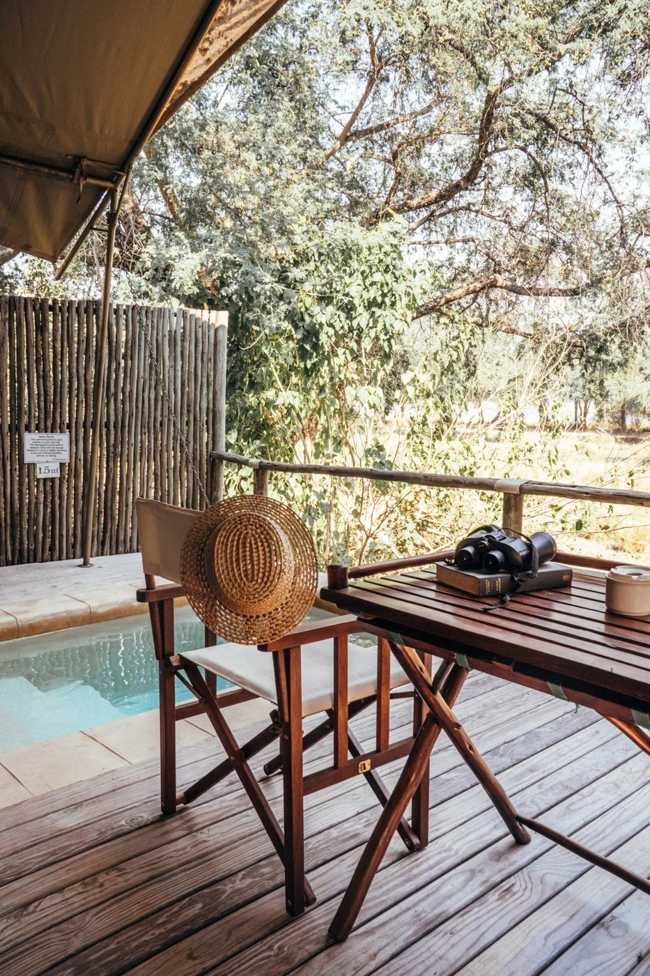 Wooden deck with two chairs and a small plunge pool sits under leafy trees, with sunlight dappling boards.