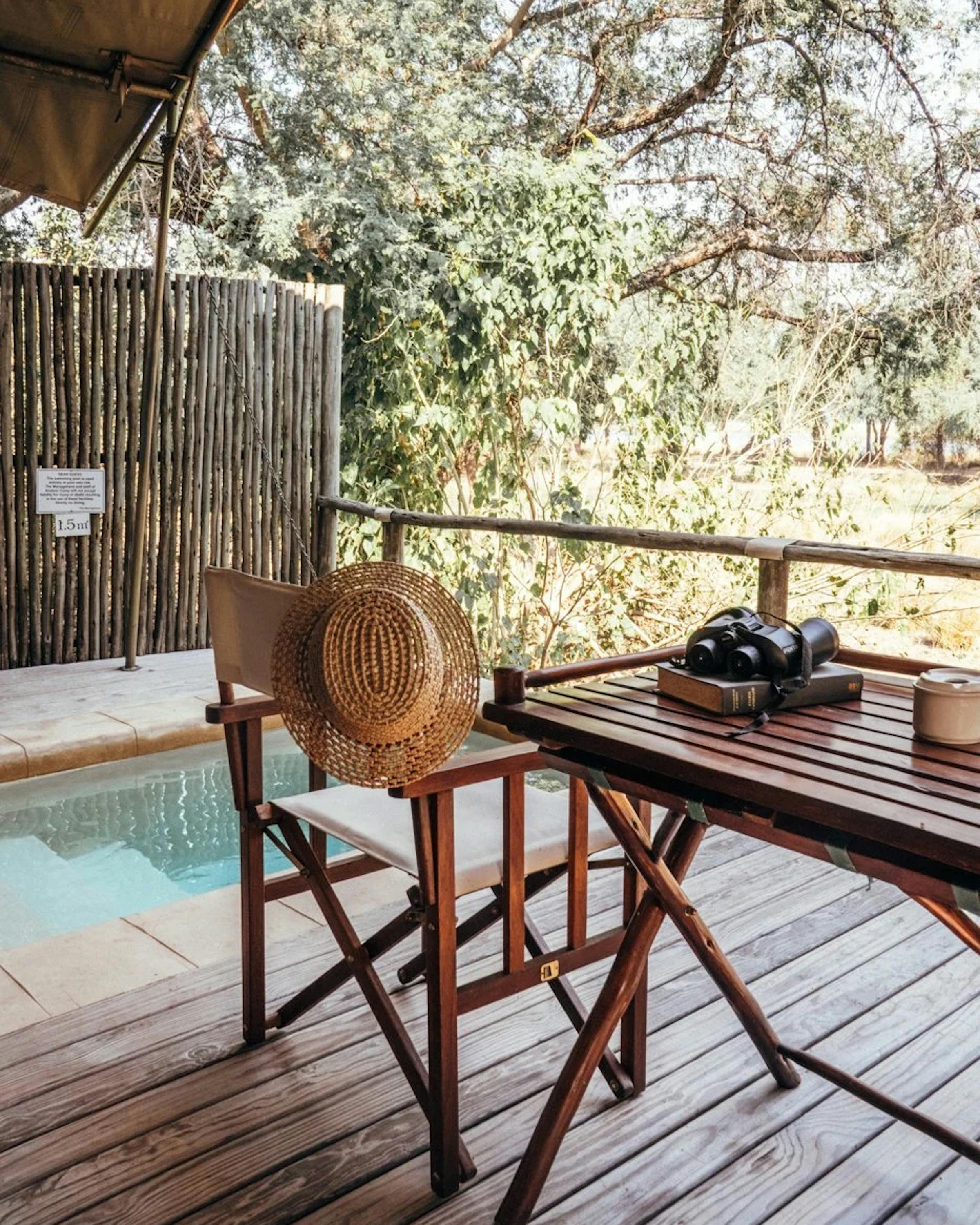 Wooden deck with two chairs and a small plunge pool sits under leafy trees, with sunlight dappling boards.