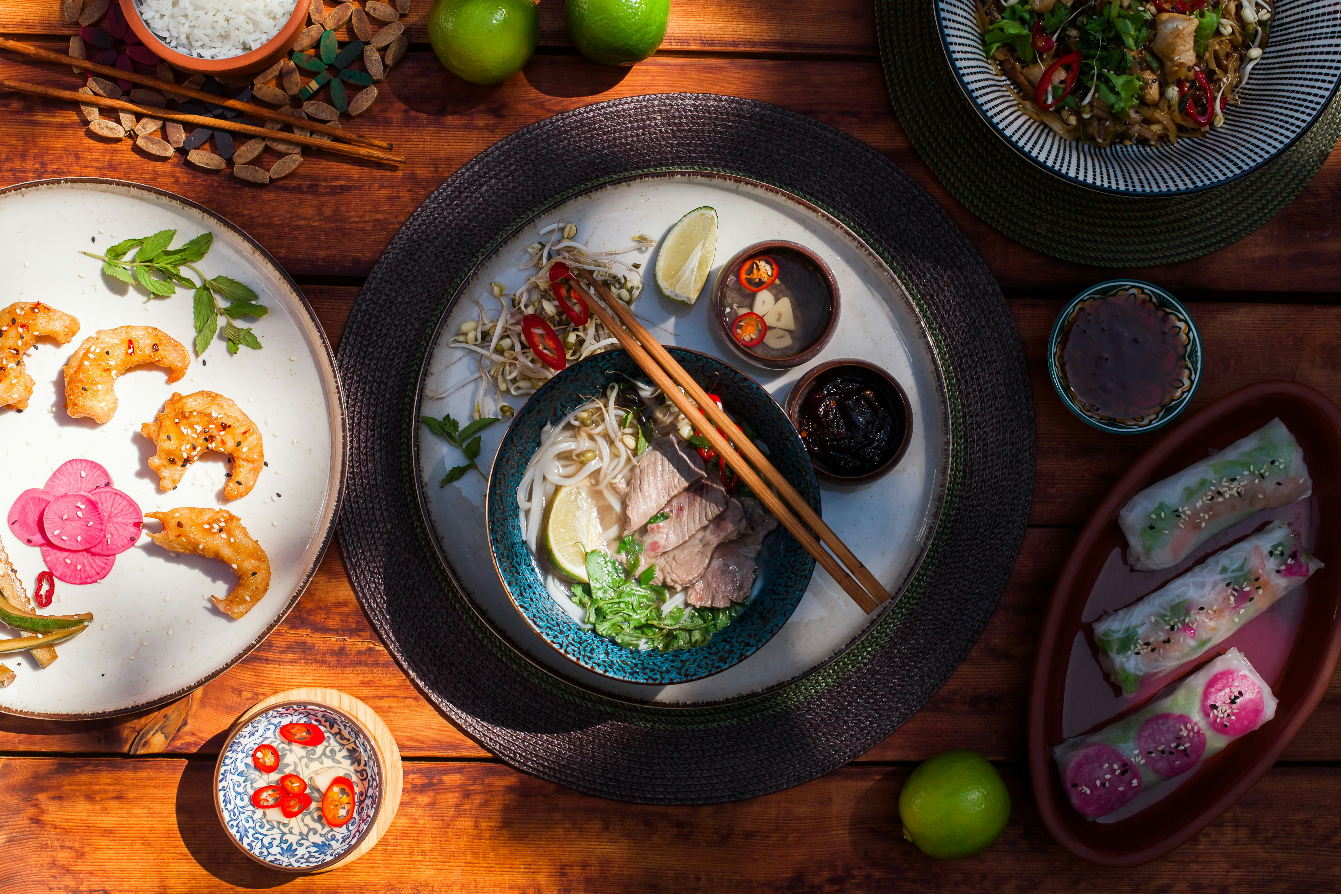Overhead view of a meal with bowls, herbs, and chopsticks on a wooden table.