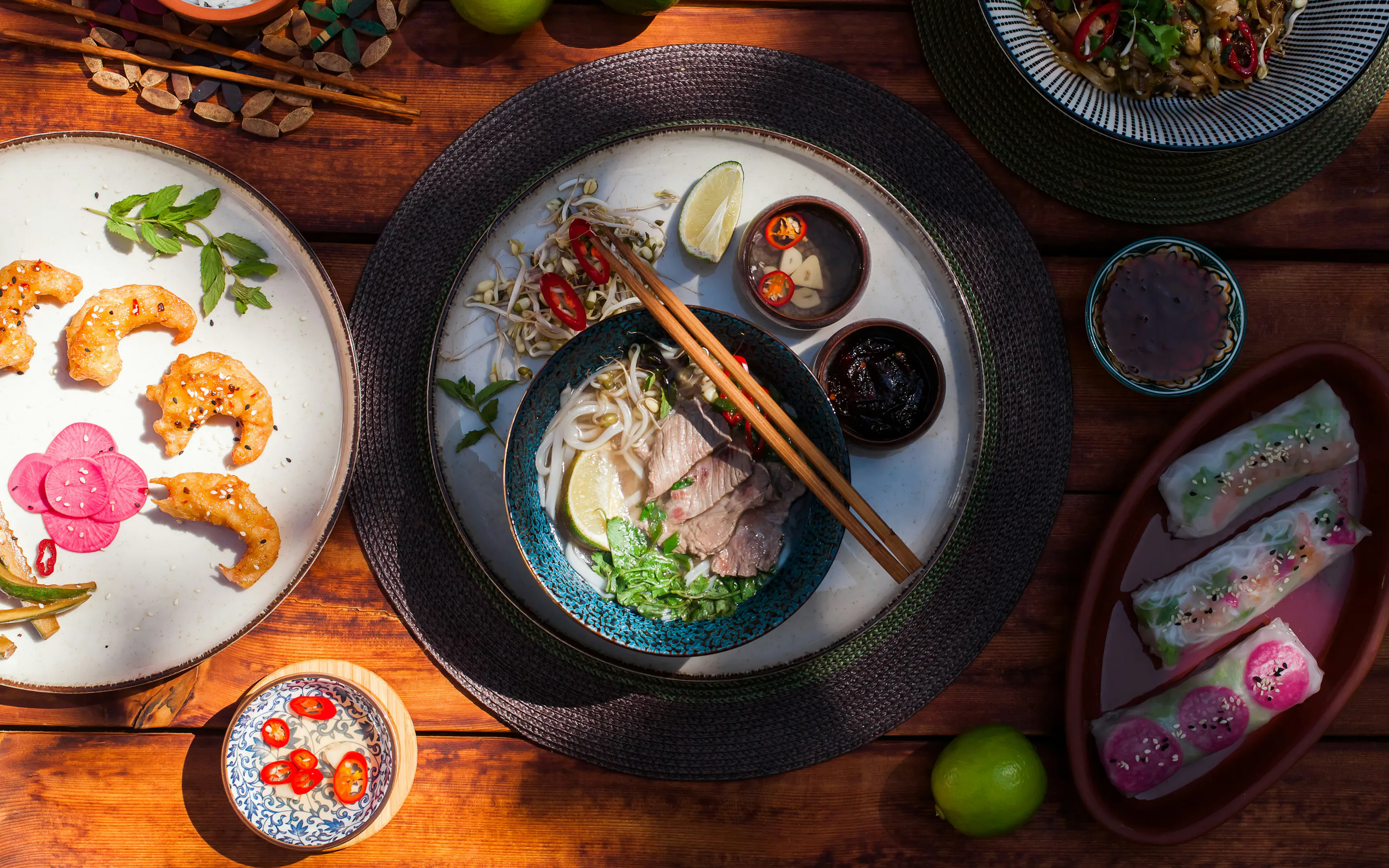 Overhead view of a meal with bowls, herbs, and chopsticks on a wooden table.