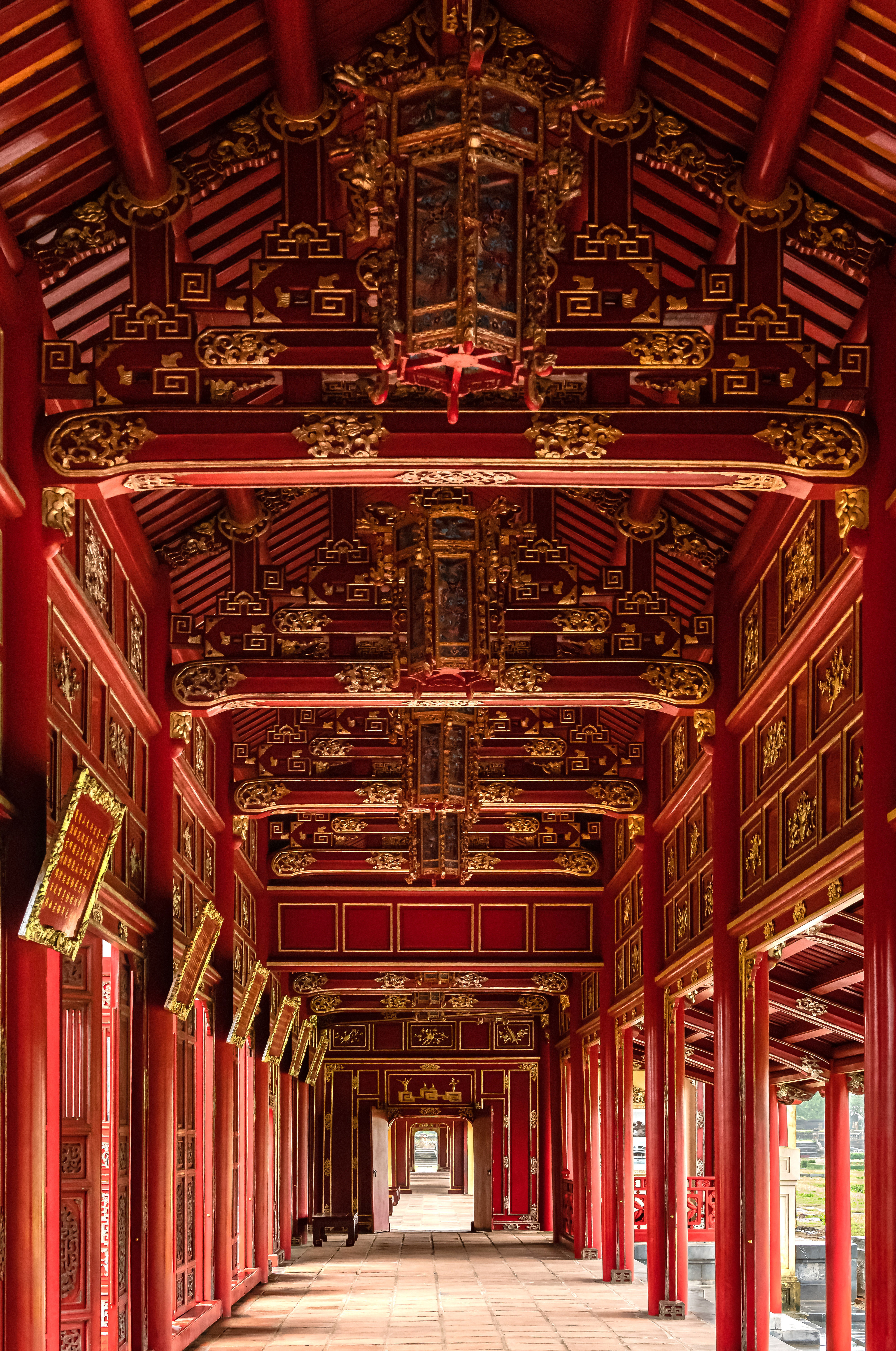 Empty corridor with red pillars and ornate painted ceiling recedes into the distance.