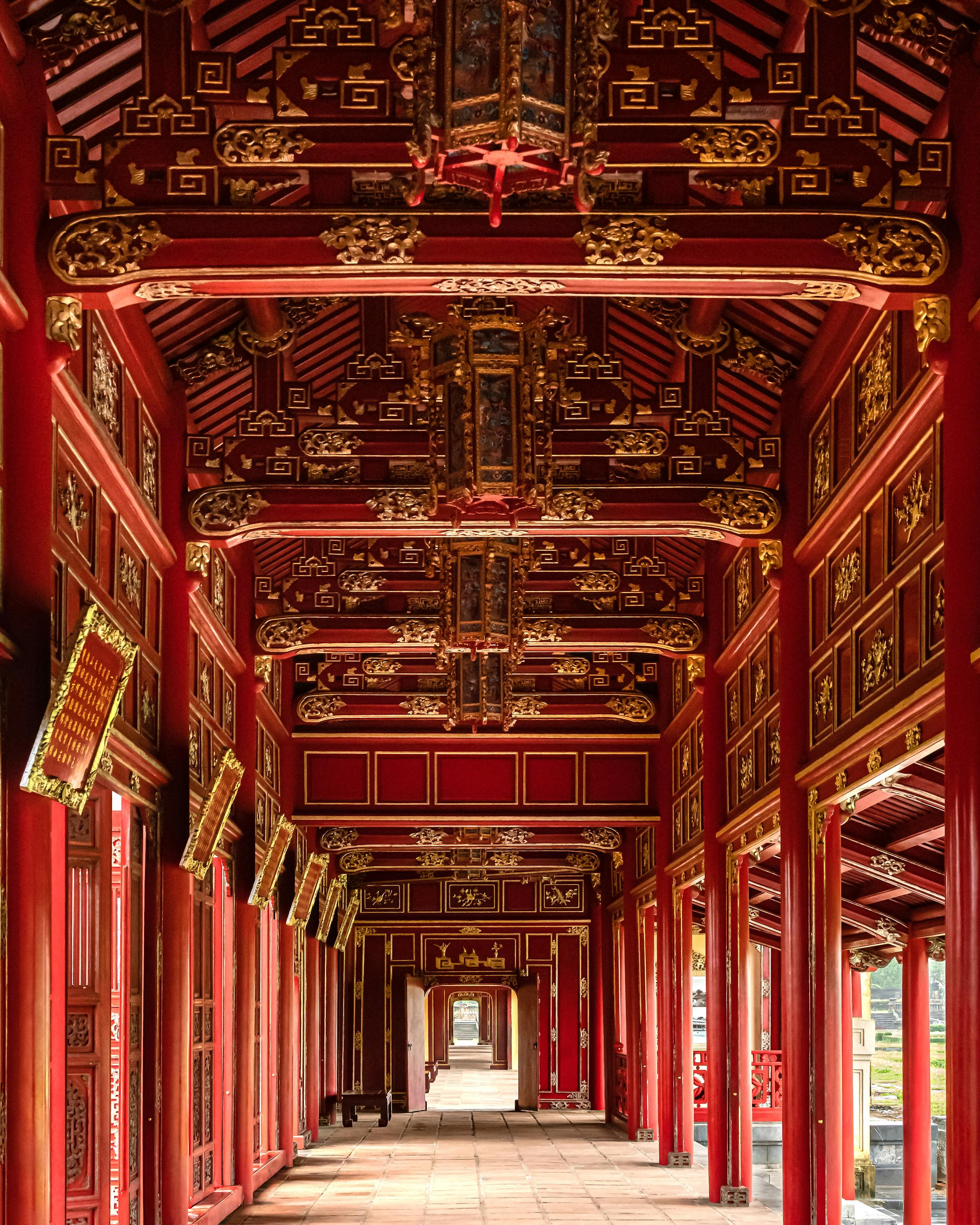 Empty corridor with red pillars and ornate painted ceiling recedes into the distance.
