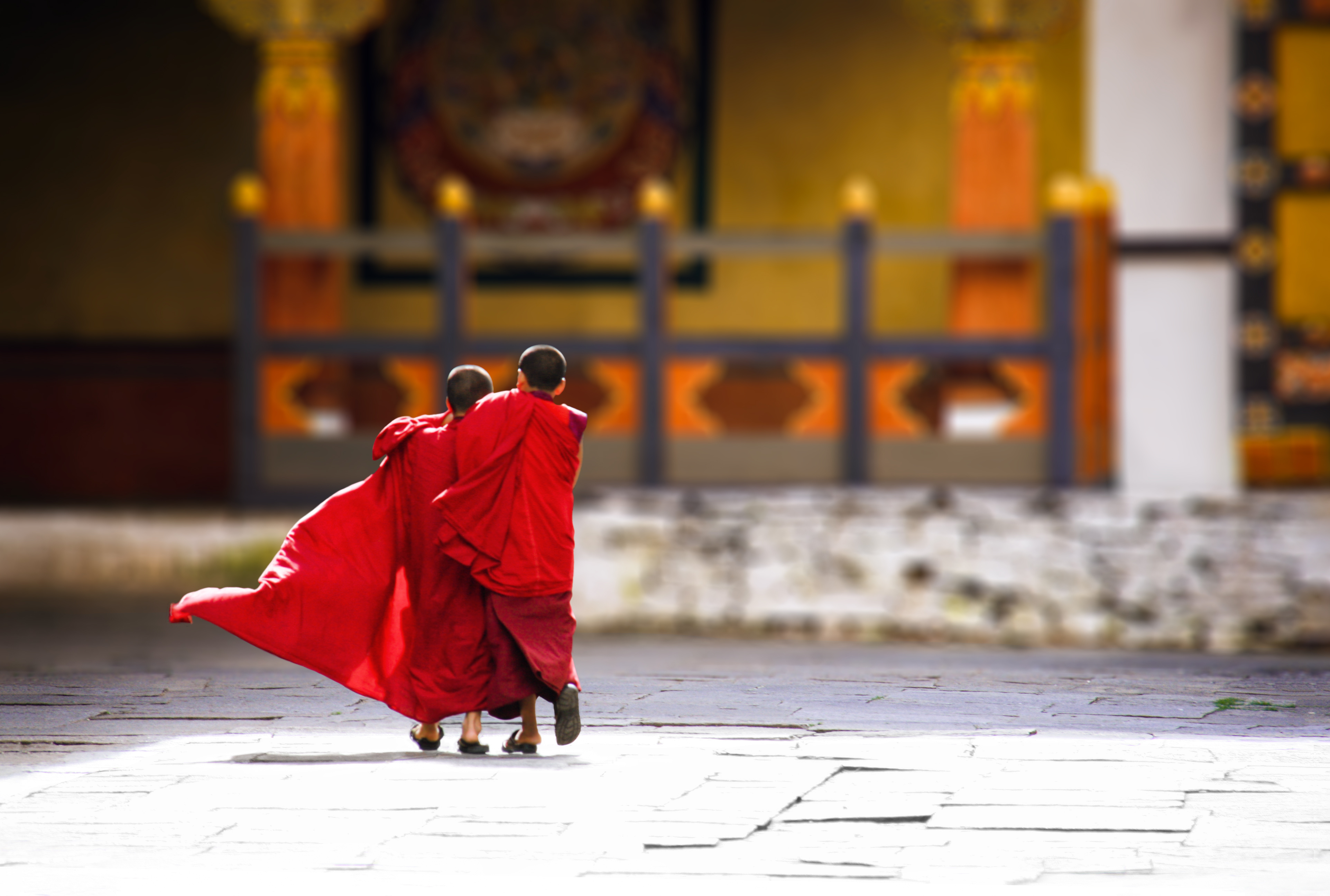 Two people in red robes walk across a stone courtyard with a red cloak billowing.