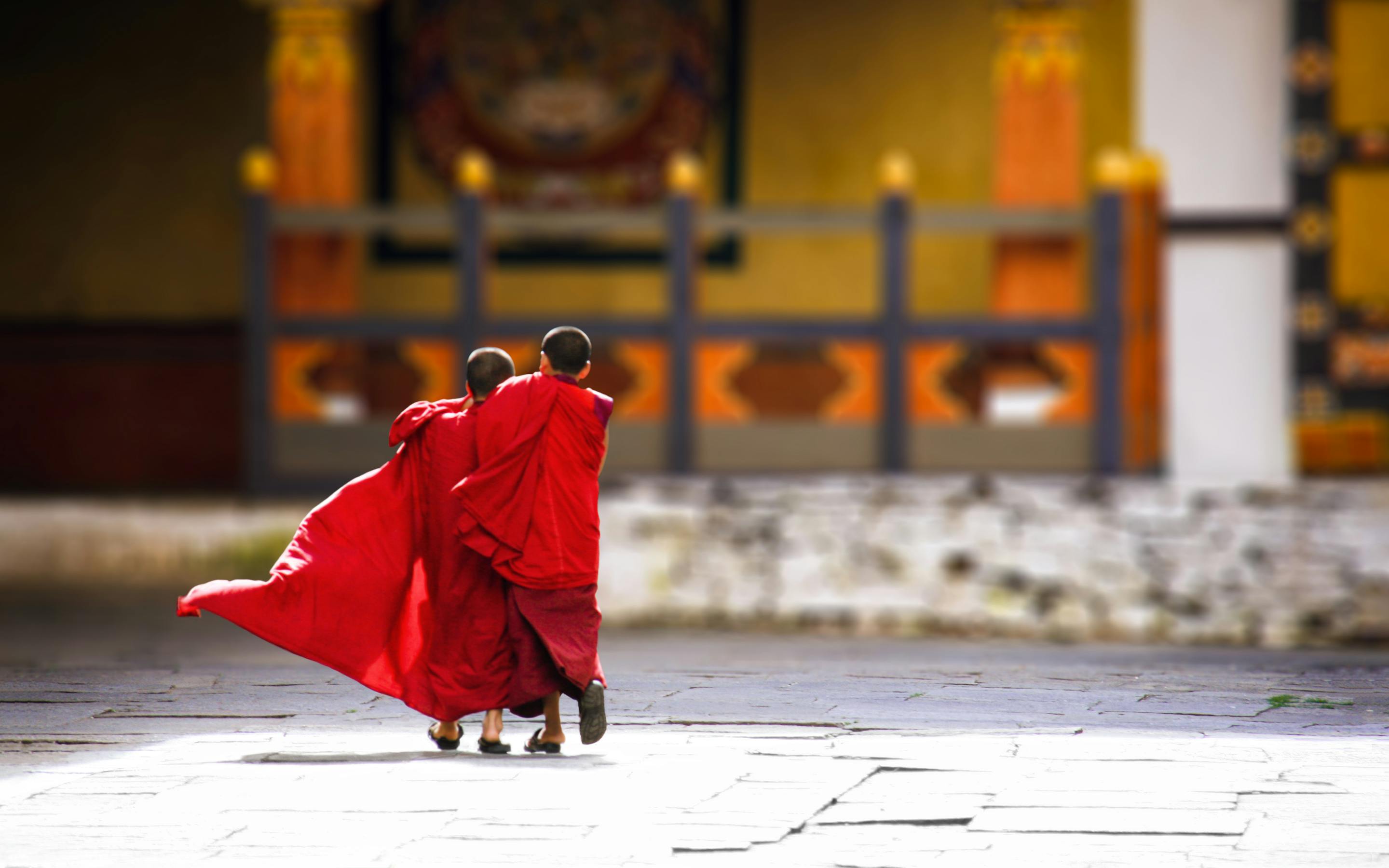 Two people in red robes walk across a stone courtyard with a red cloak billowing.